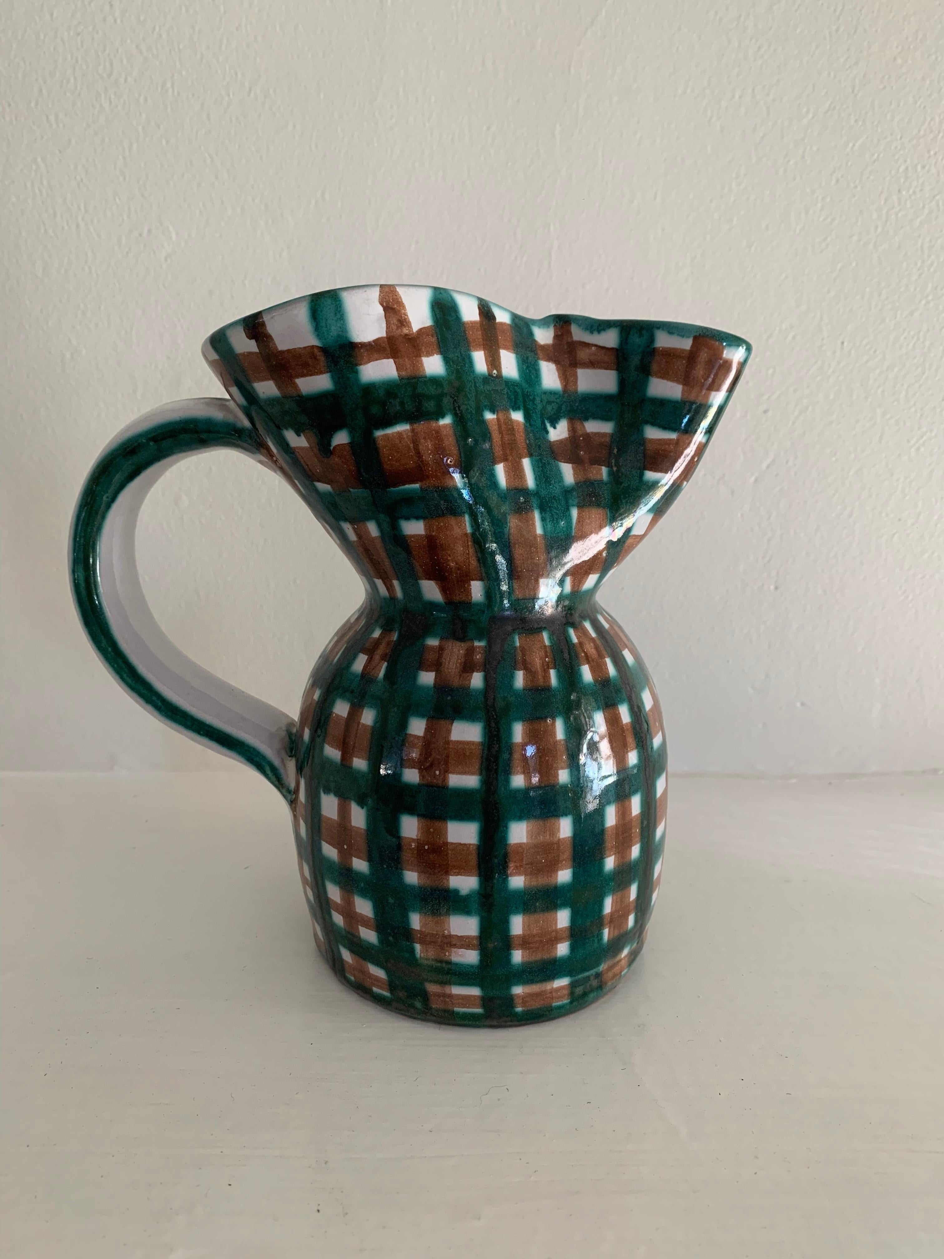 Una straordinaria brocca in ceramica realizzata a mano dal ceramista francese Robert Picault, con il suo iconico motivo a quadri in verde intenso e marrone su fondo bianco. L'ampio labbro svasato e l'ampio manico evidenziano il caratteristico mix di