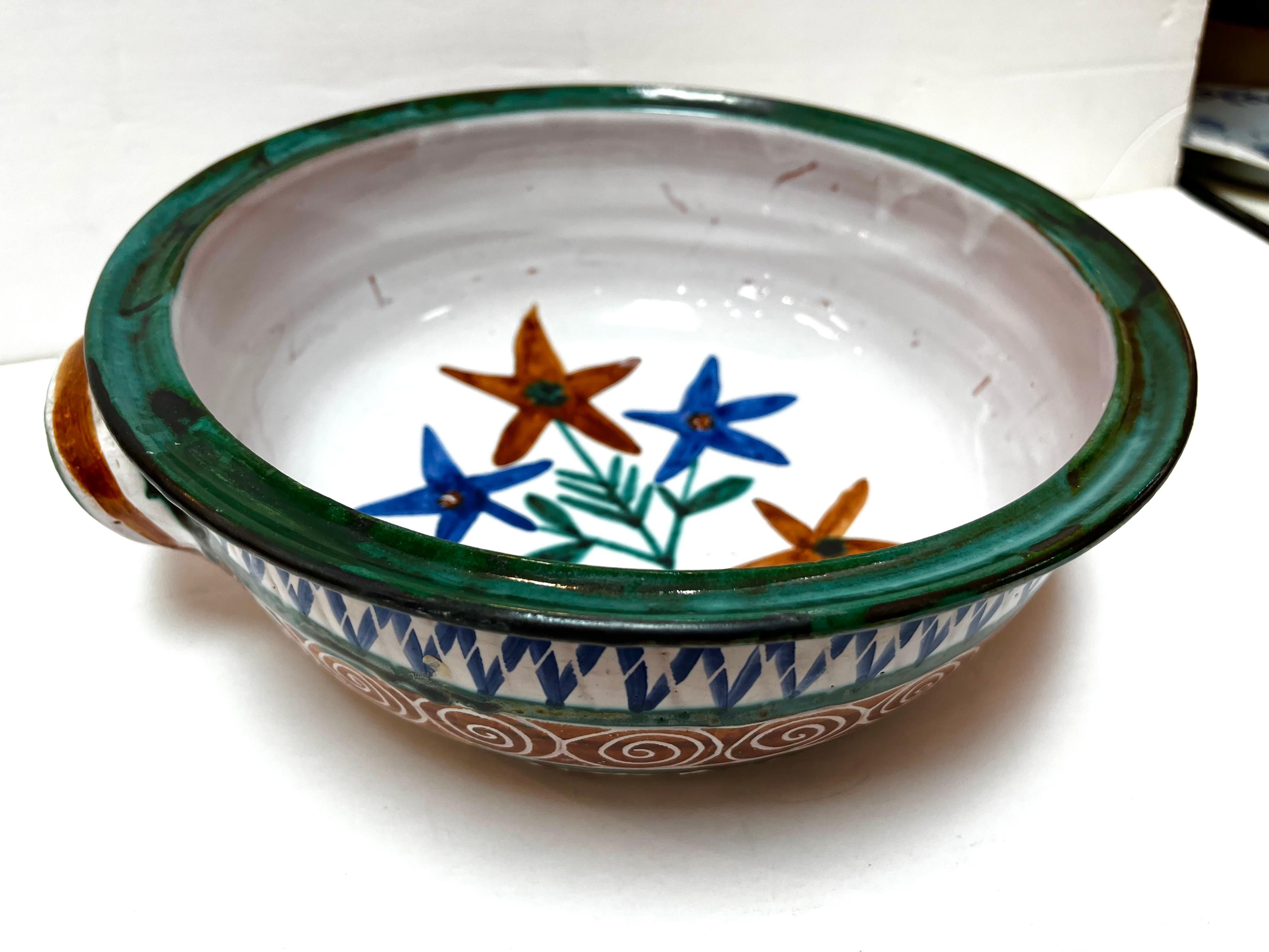 A large, double handled mid century hand painted ceramic dish by French artist Robert Picault. This dish features various geometric designs on the outside and a floral design on the inside. From the studio pottery website, “Robert Picault was born