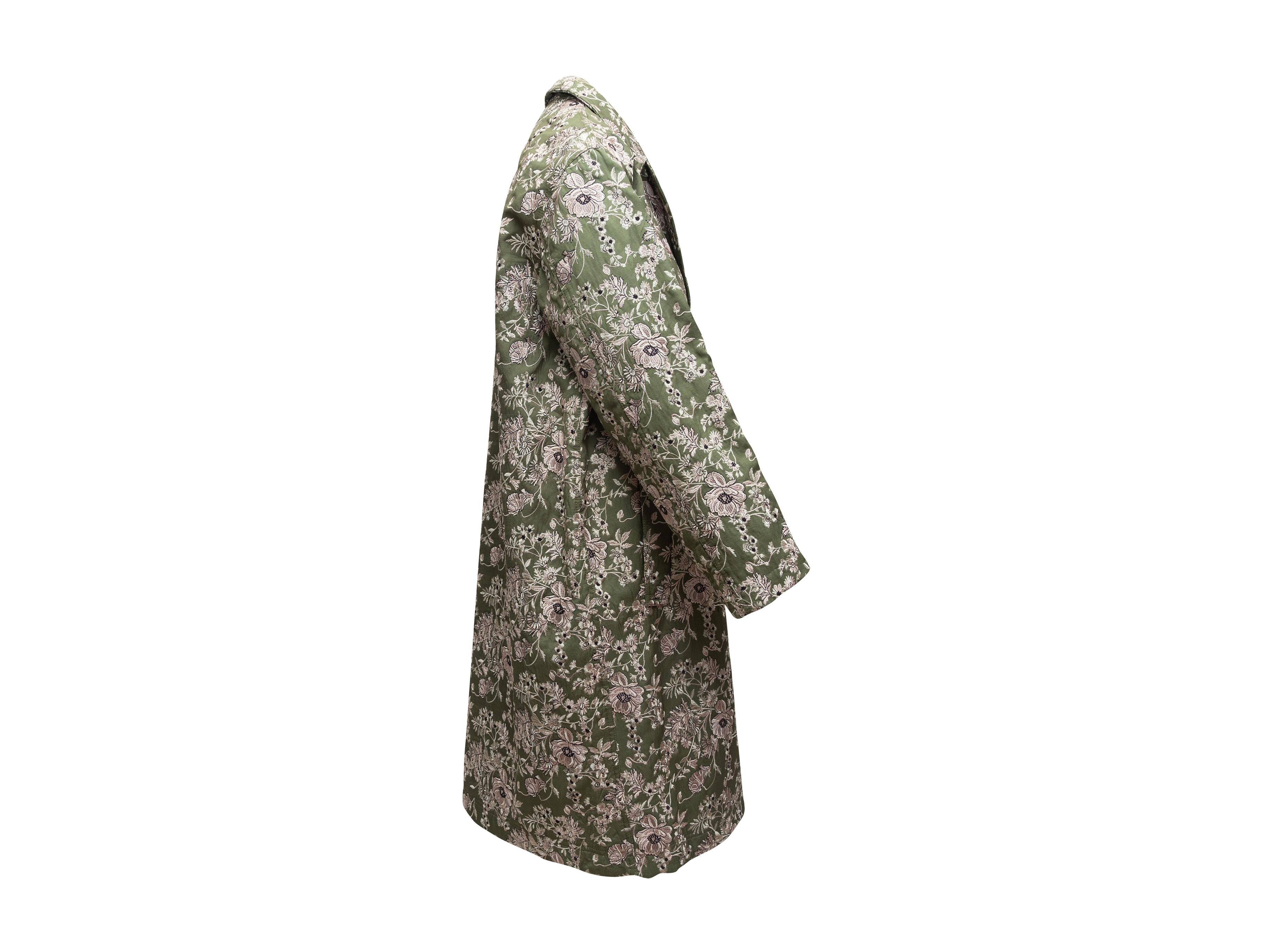 Product details: Olive green, cream and black long jacquard coat by Robert Rodriguez. Floral pattern throughout. Peaked lapel. Dual hip pockets. Button closures at front. 46