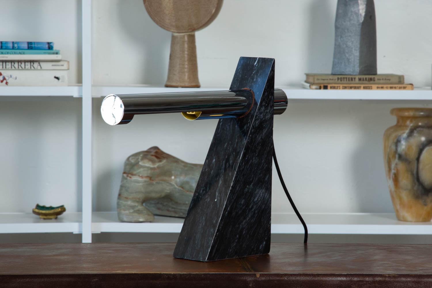 A Postmodern chrome and marble table lamp by Robert Sonneman for George Kovacs, circa 1980s. The sculptural lamp features a solid triangular shaped piece of black marble with a cantilevered chrome tube, that houses the bulb and extrudes from both