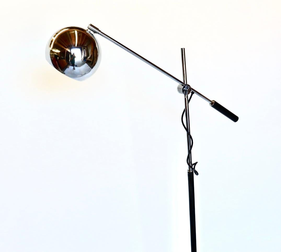 Robert Sonneman eyeball floor lamp circa 1960s, USA. The lamp features a chrome sphere shade on a pivoting arm that can be adjusted to multiple vertical heights with cylindrical black handle. The stem of the lamp is a narrow chrome and black