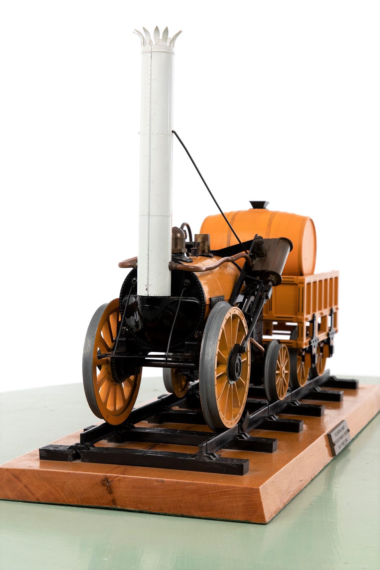 An intricately built to-scale model of Robert Stephenson’s famous 1829 Rocket train. The model Rocket locomotive and coach sit upon a section of railway track. This particular model was gifted in 1984 and comes with a brass plaque to the front. A