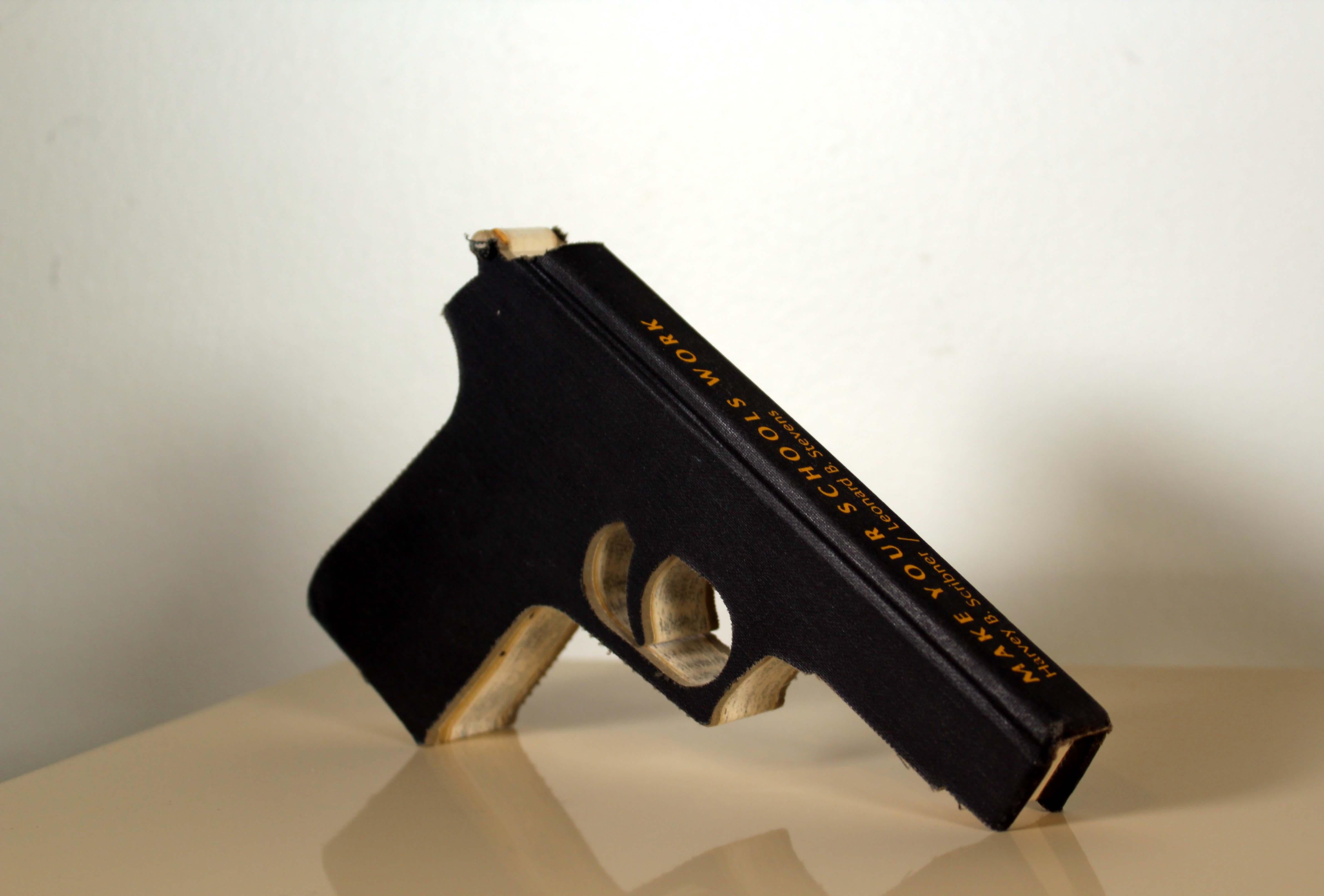 An imaginative hand cut book sculpture in the shape of the gun by California based artist Robert The. Hand signed in ink by artist with a 1996 date. Robert The is known for making sculptures from books, often culled from dumpsters and thrift store