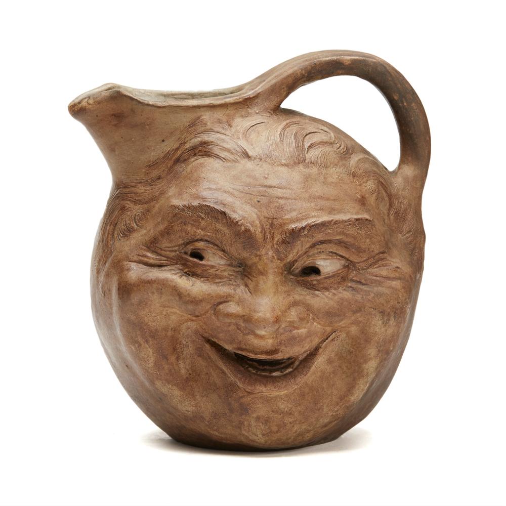 A rare Martin Brothers extra large stoneware face jug by Robert Wallace Martin dated 1897 sculpted in relief with a grinning face exposing teeth and a blowing or whistling face to the opposite side. With a large pouring spout and raised loop handle