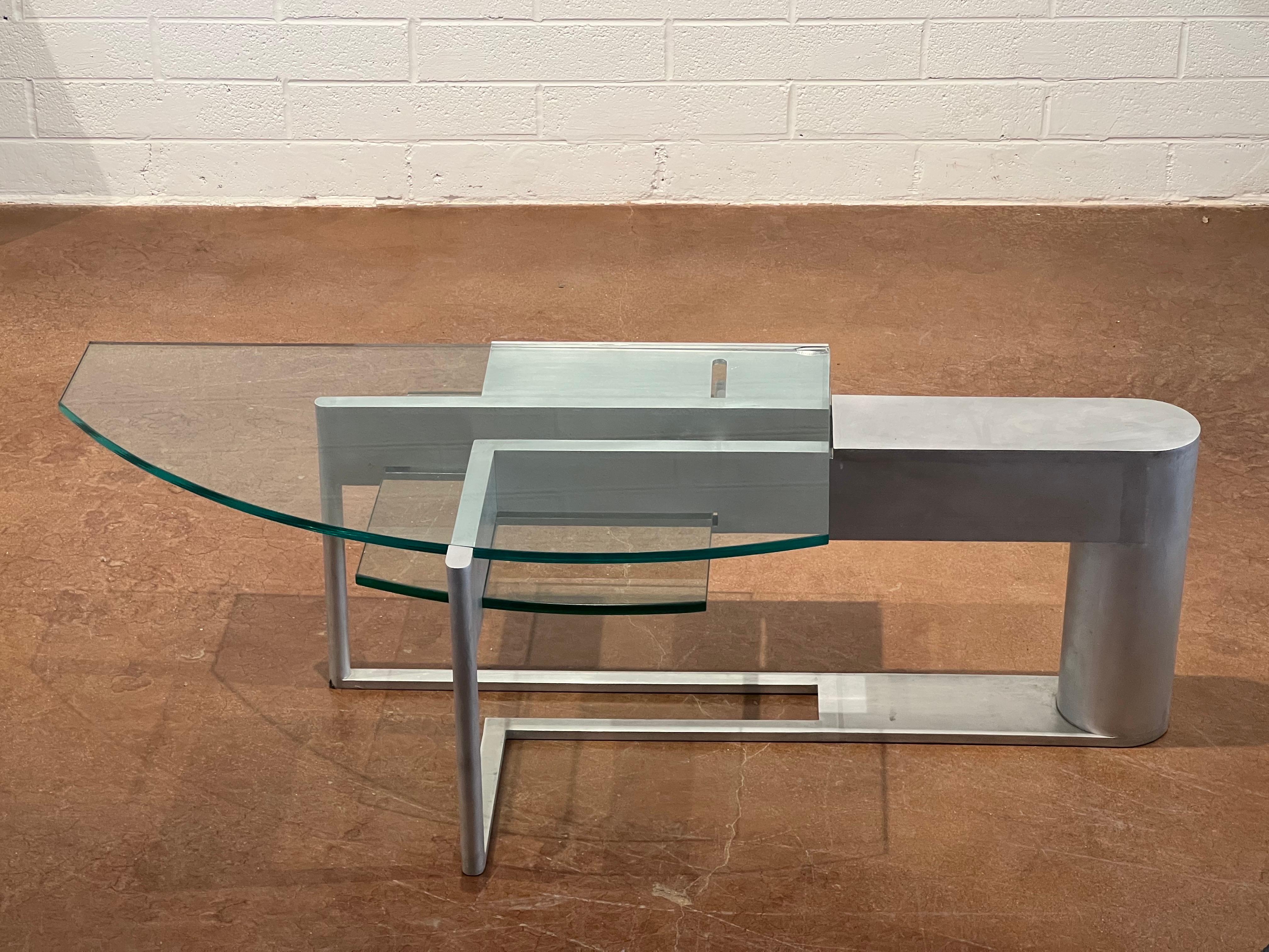 This Robert Whitton coffee table, crafted from aluminum and glass, is a striking example of design excellence from the late 20th century. Produced during the 1980s and early 1990s, the table exemplifies the era's innovative use of industrial