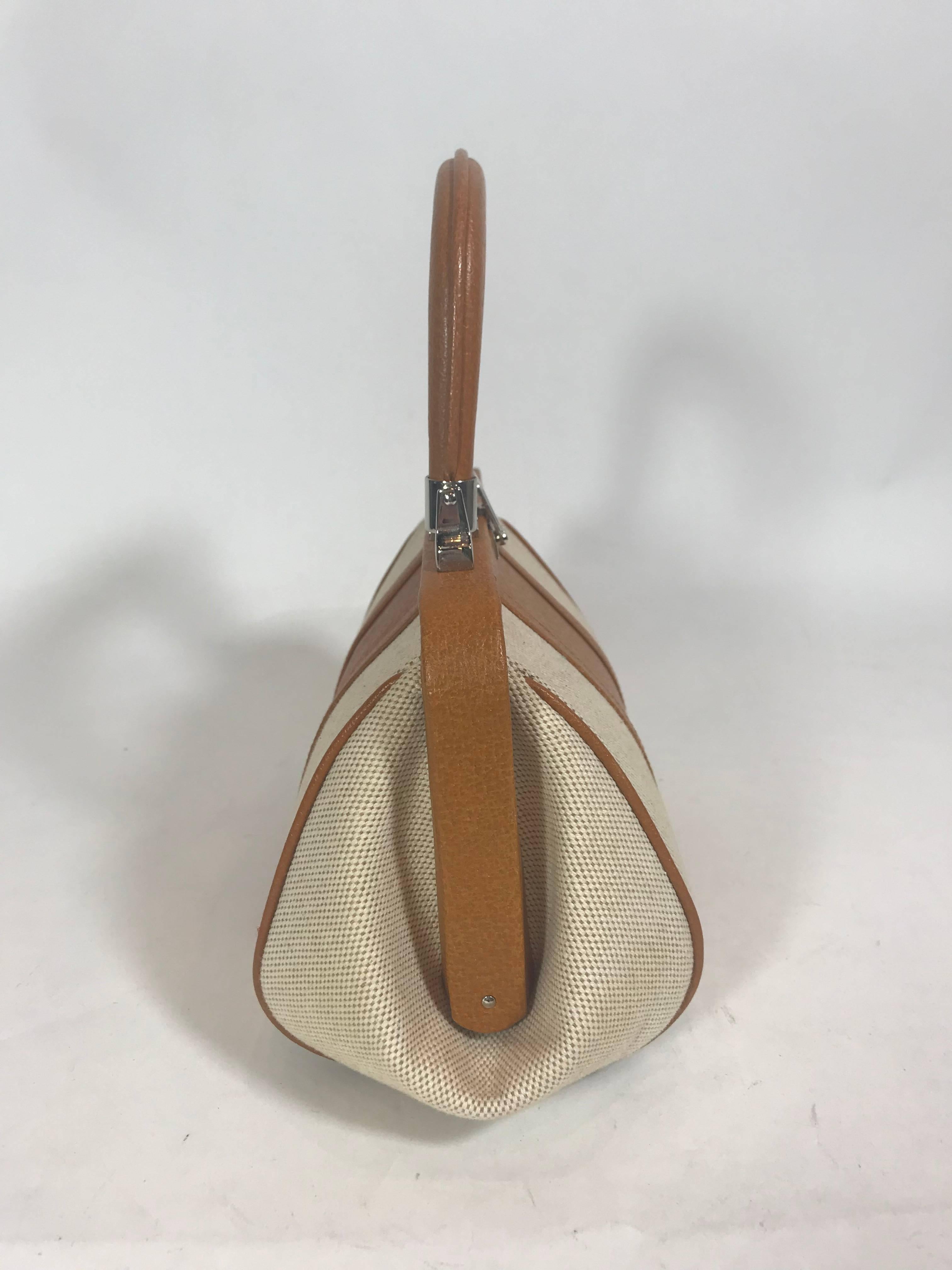 Canvas and camel leather.
Silver-tone hardware.
Push-lock closure at top.
Single flat top handle.
Leather trim.
Leather lining.
Dual pockets at interior wall; one with zip closure.