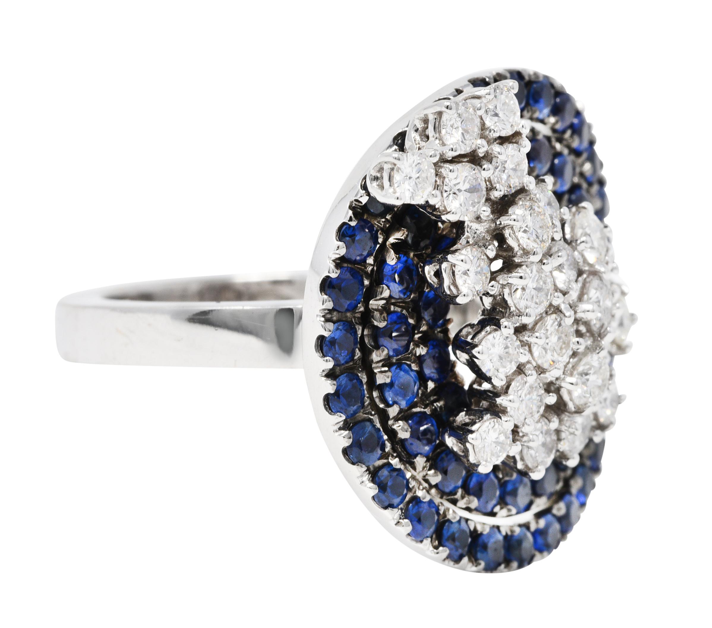 Designed as concentric circles of prong set sapphires with a black rhodium finish

Very well matched with vibrant royal blue color while weighing approximately 2.10 carats total

Centering a dynamic cluster of round brilliant cut diamonds

Weighing