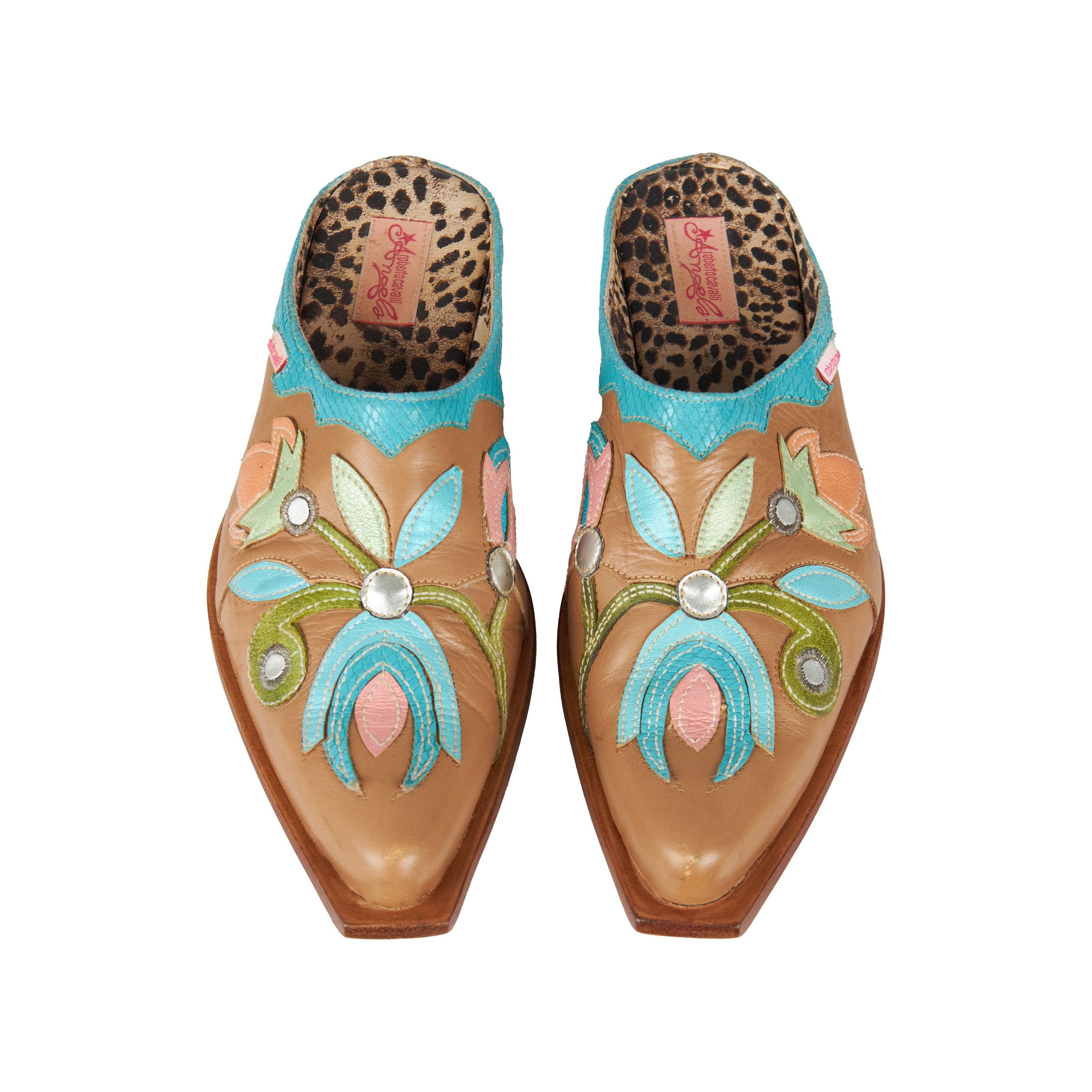 These Roberto Cavalli Angels mules bring the perfect blend of classic style and fashion-forward attitude. Crafted from a light brown leather, they feature an intricate flower pattern appliqué in multicolor and stacked cuban heel. The signature