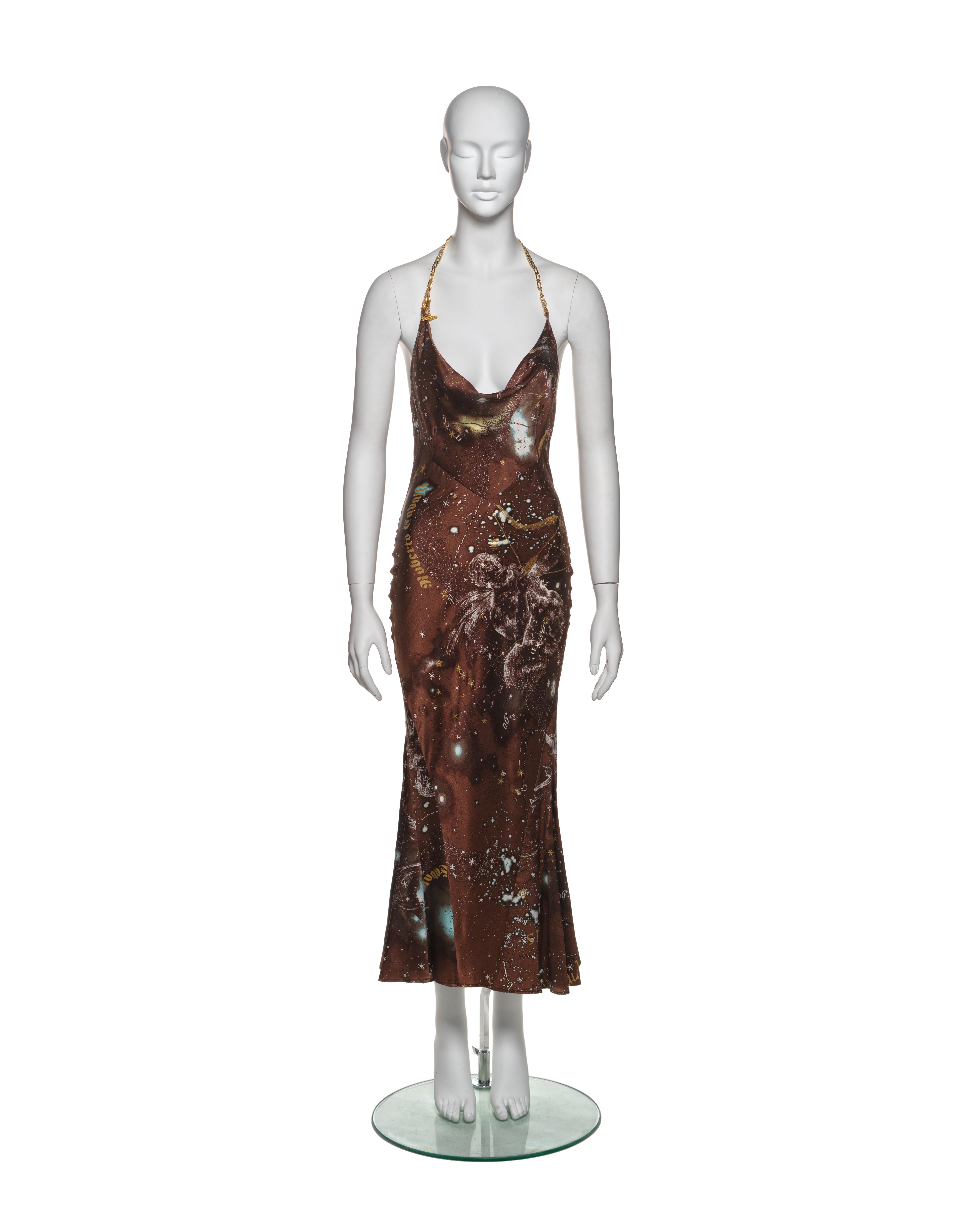 This Roberto Cavalli silk dress features a halter neckline with gold chain straps. The fabric showcases a rich brown base with intricate astrological-themed prints, including constellations, stars, and zodiac symbols. The cowl neckline drapes