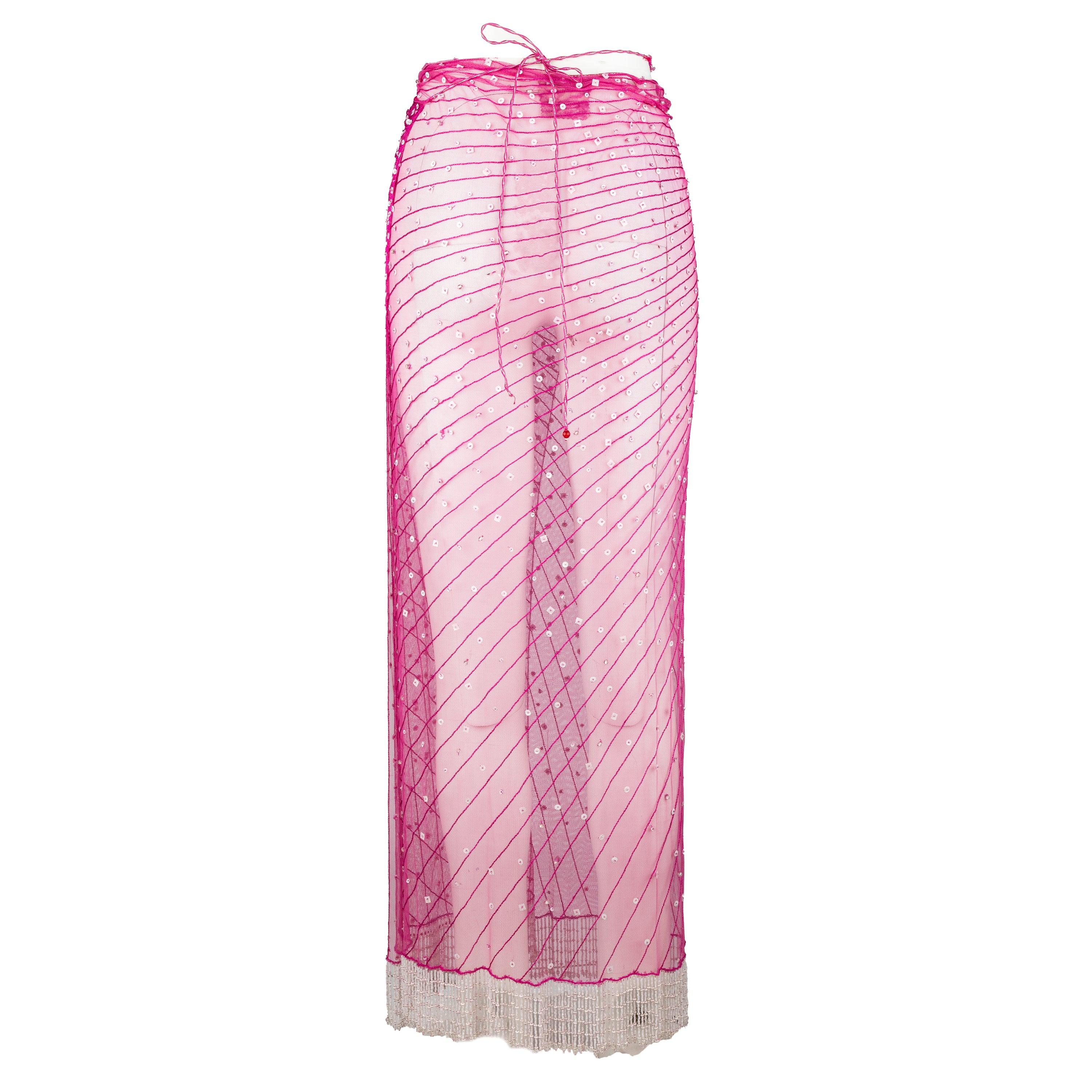 Expertly crafted by iconic designer Roberto Cavalli, this fuchsia pink wrap skirt is a must-have for any fashion-forward individual. Made with see-through fabric, this skirt is embellished with intricate beads and features a unique slanted pattern.