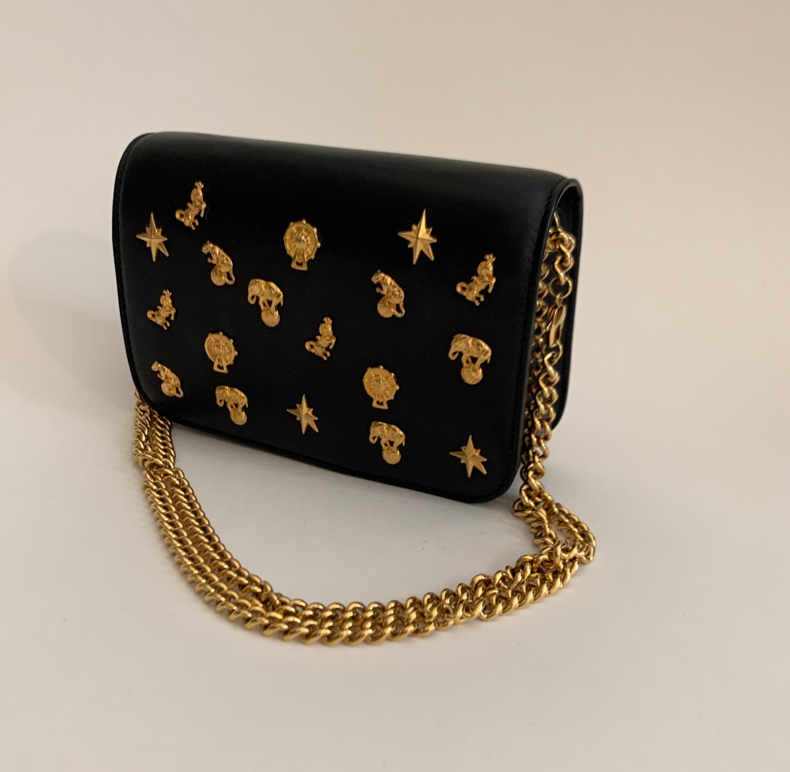 Roberto Cavalli circus bag in black leather with gold tone hardware. Gold detail on front features Ferris wheels and circus animals including elephants, leopards, and horses. Removable gold chain strap that can be worn long or doubled. Lined in a