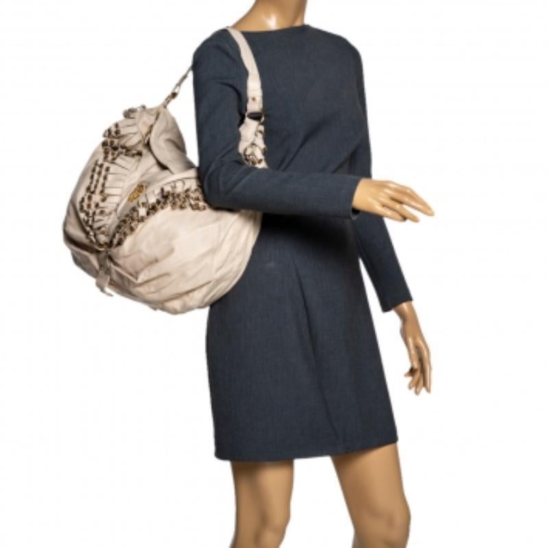 Ce sac hobo de Roberto Cavalli est un ajout remarquable à votre collection. Confectionné en cuir crème, il est décoré de clous et de franges. Confectionné en Italie, ce hobo est doté d'une bandoulière et du logo de la marque en ton or. La fermeture