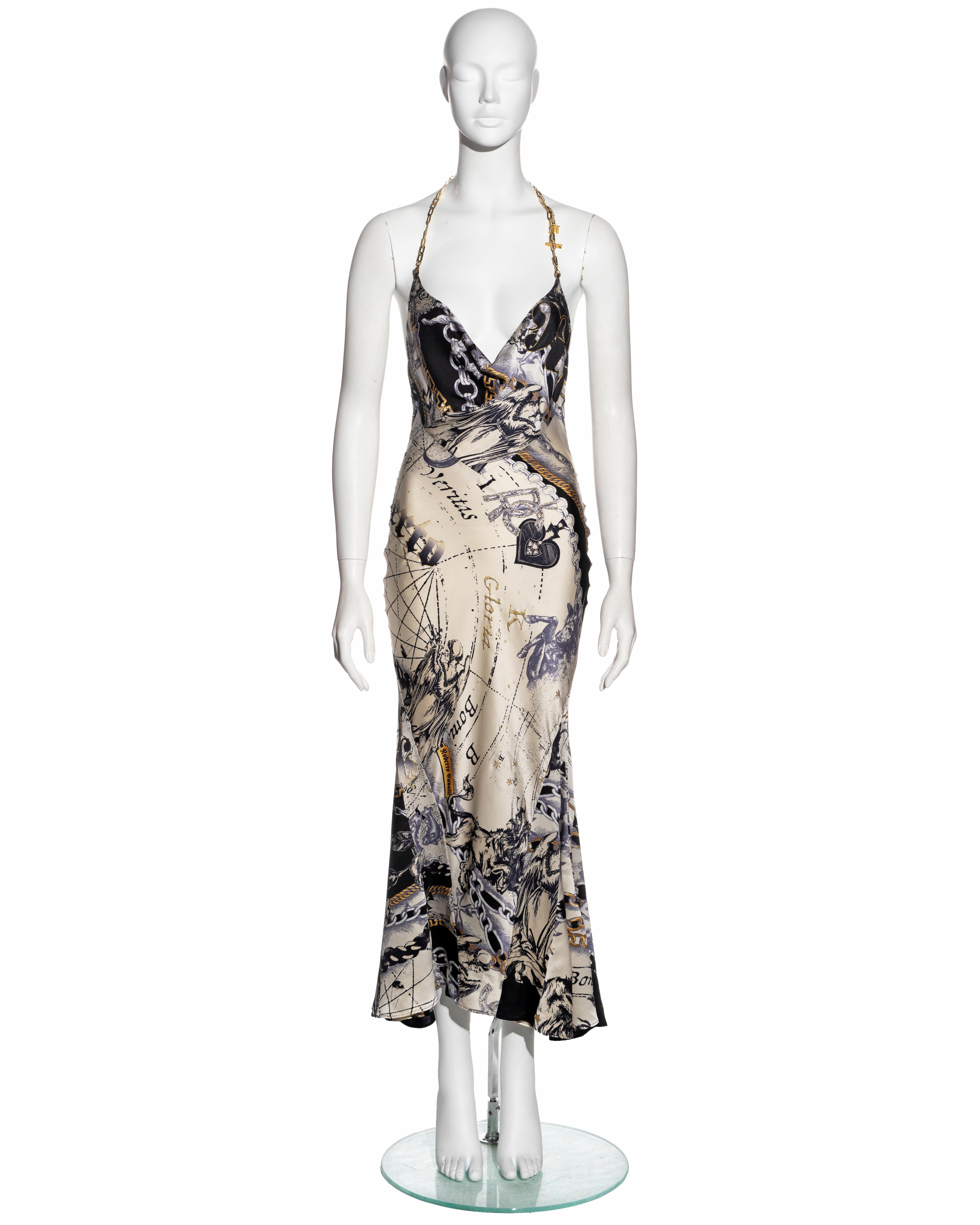 ▪ Roberto Cavalli evening dress  
▪ Sold by One of a Kind Archive 
▪ Constructed from bias-cut cream silk with a zodiac print featuring imagery of chains and roses
▪ Gold-tone metal chain halter-neck with two charms 
▪ Cowl neck 
▪ Size Small
▪