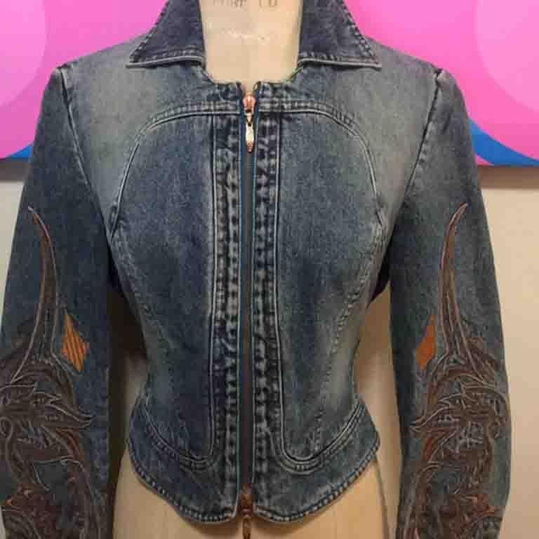 This unique vintage denim jacket by Roberto Cavalli is a real find. As wearable today as when it was made! Pair with white or blue skinny jeans for a great look. unique brown embroidered sleeves and leather braided lac tie in the back to pull in the