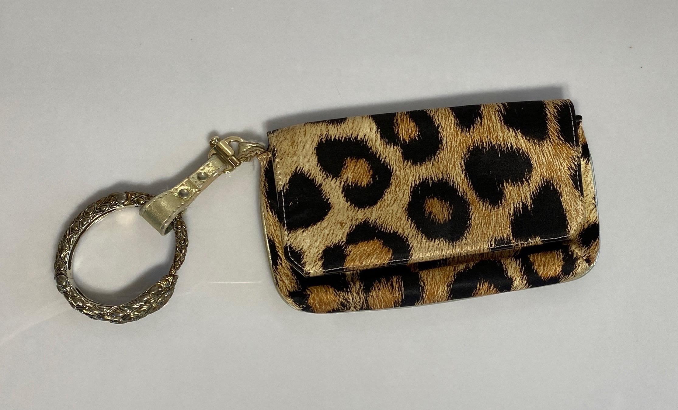 The Roberto Cavalli Leopard Silk Print Bracelet Bag is a gold and brown leopard silk print clutch bag with gold leather piping with a removable gold/bronze serpent bracelet as handle. The removable handle has a gold clasp, a gold leather strap that