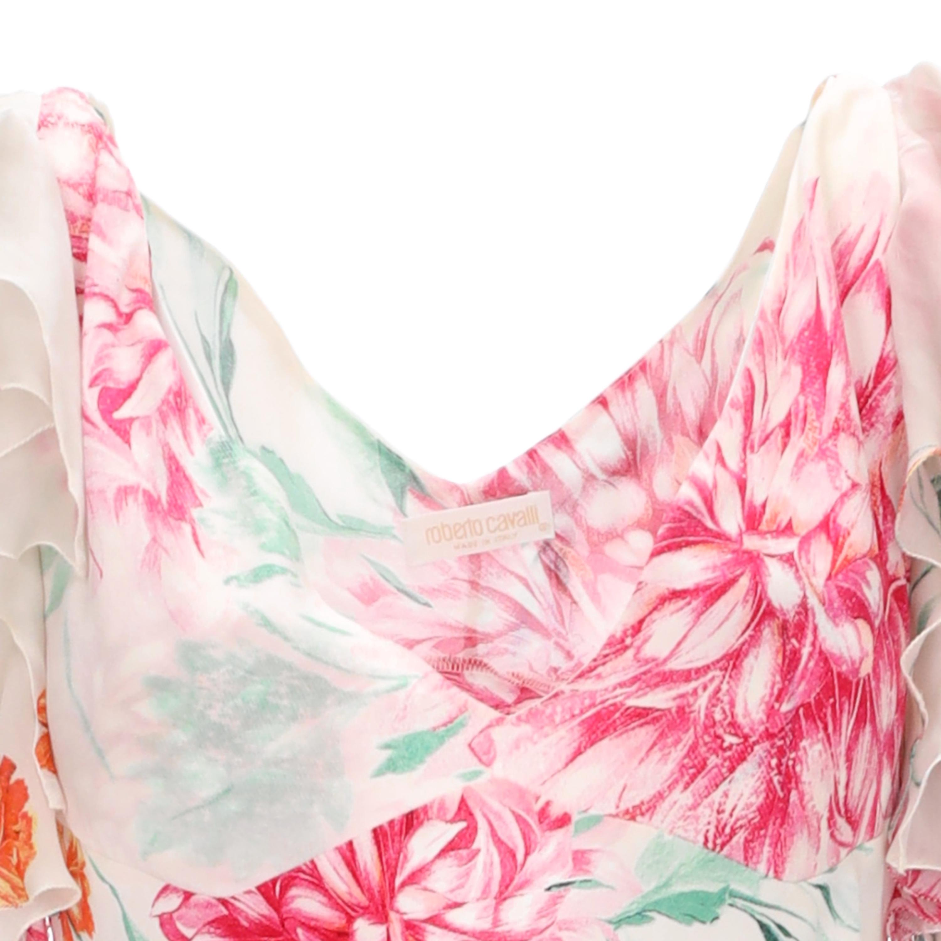 This Roberto Cavalli dress is crafted from luxurious light silk and features a vibrant floral pattern with pink and orange flowers complemented by hints of green leaves. The frilled sleeves and plunging V-neck accentuated by a long, graceful hemline