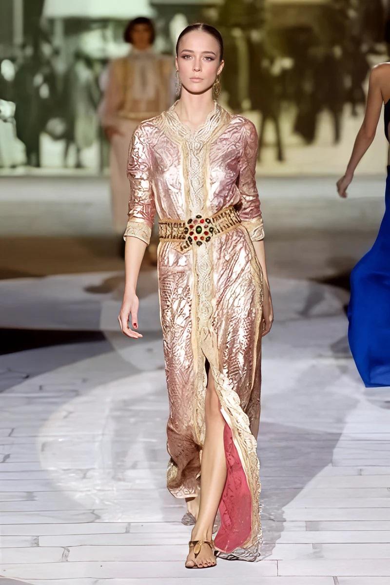 This breathtaking long coat is crafted from intricate lace and adorned with delicate gold embroidery, with laser cut details all over this dress. The scalloped edges and detailed embellishments along the front and cuffs highlight its opulent design.