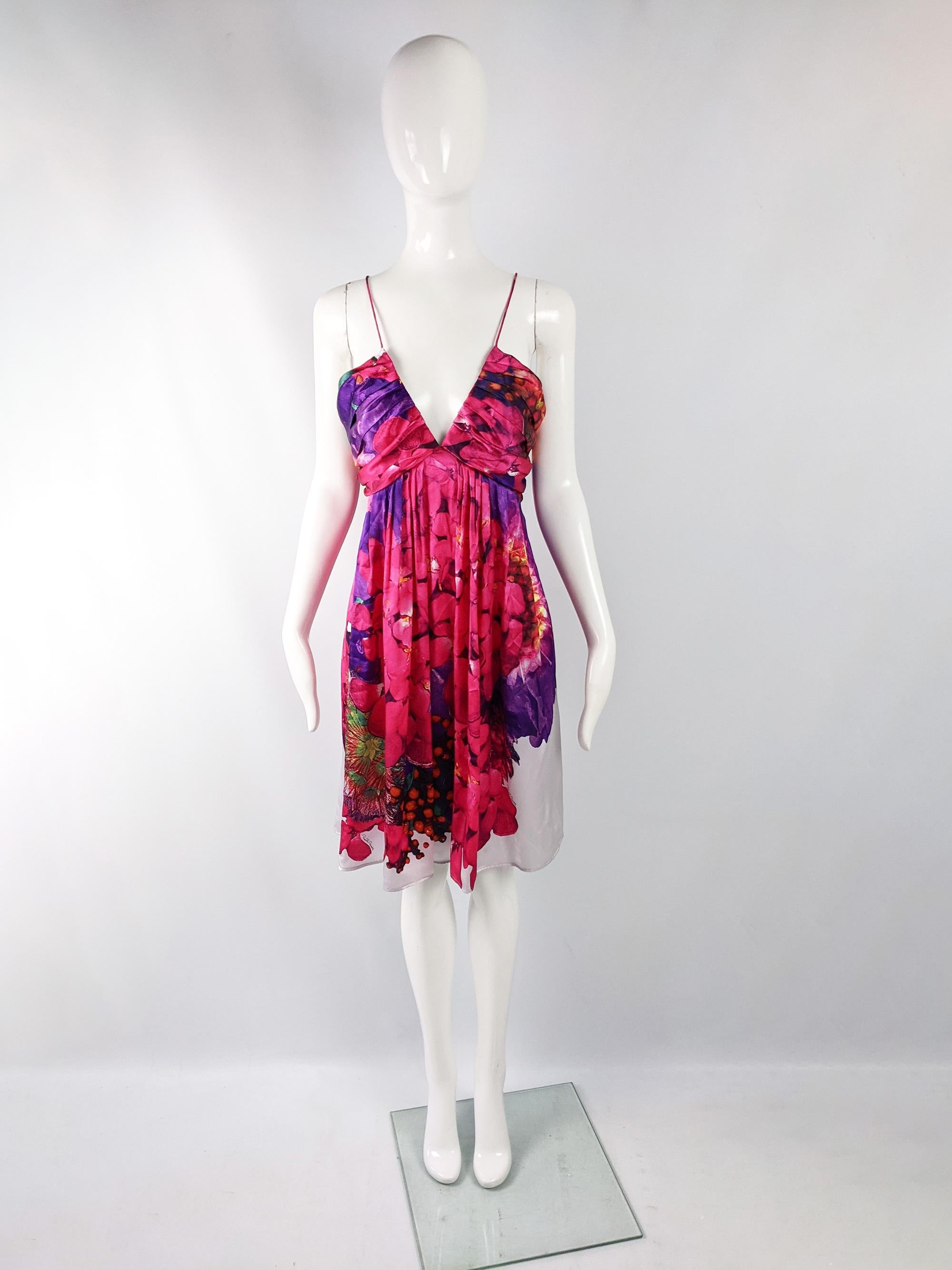 A stunning Roberto Cavalli sleeveless dress in a white and fuchsia vibrantly floral printed silk. The silhouette is so flattering with a draped, soft pleated bust with a plunging neckline, contrasting with the nipped waist and flared skirt for an