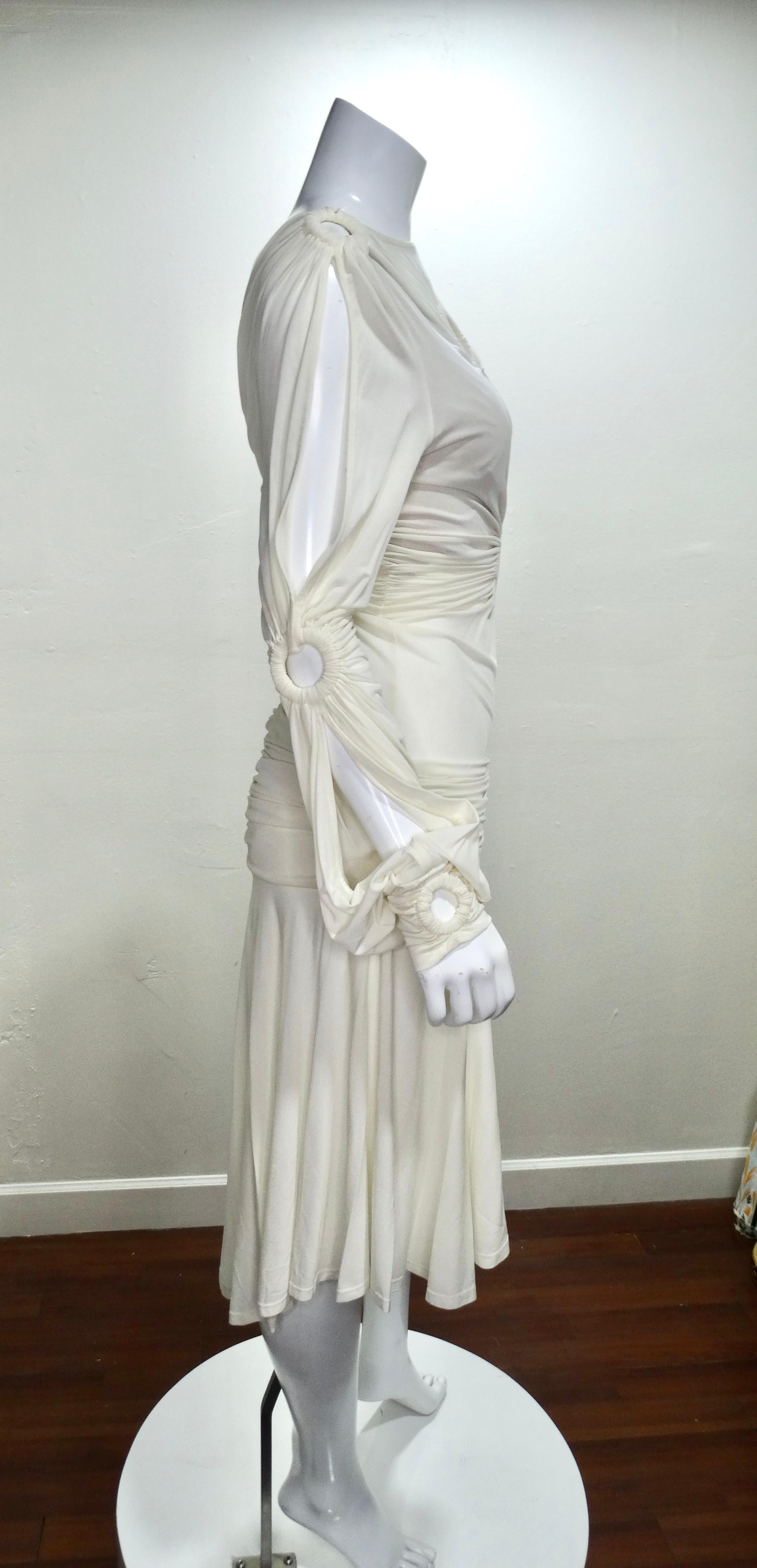 Show off in this amazing Cavalli dress! Circa 1990s, this cream dress features open o-ring details complete with   ruching throughout, an asymmetrical hem with pleating, a high neckline and a side zip closure. Slits can be found on the long sleeves,