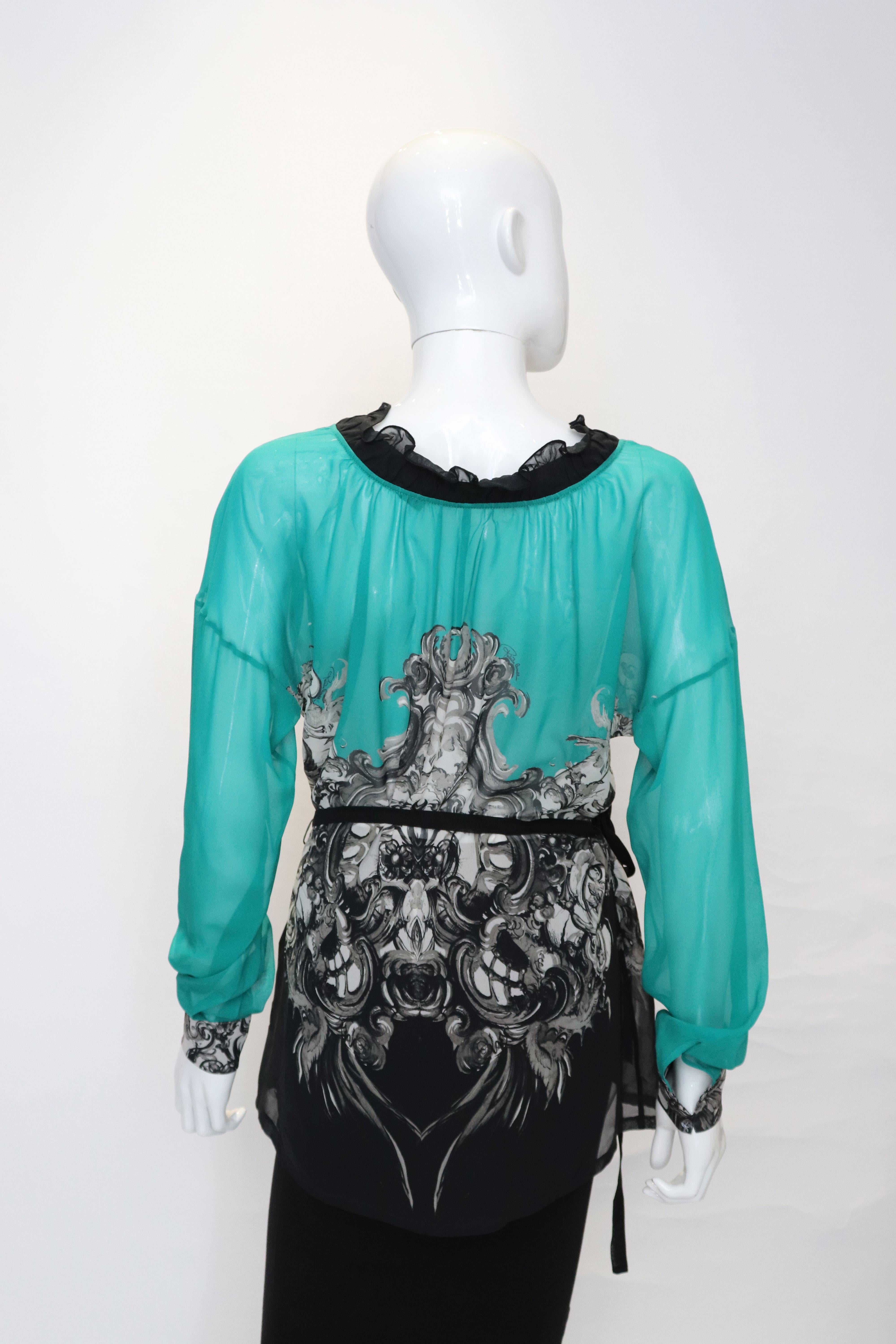 A great silk top by Roberto Cavalli. The top is emerald green and black in colour with a frill neckline and short sleeves. It has a black silk tie belt.