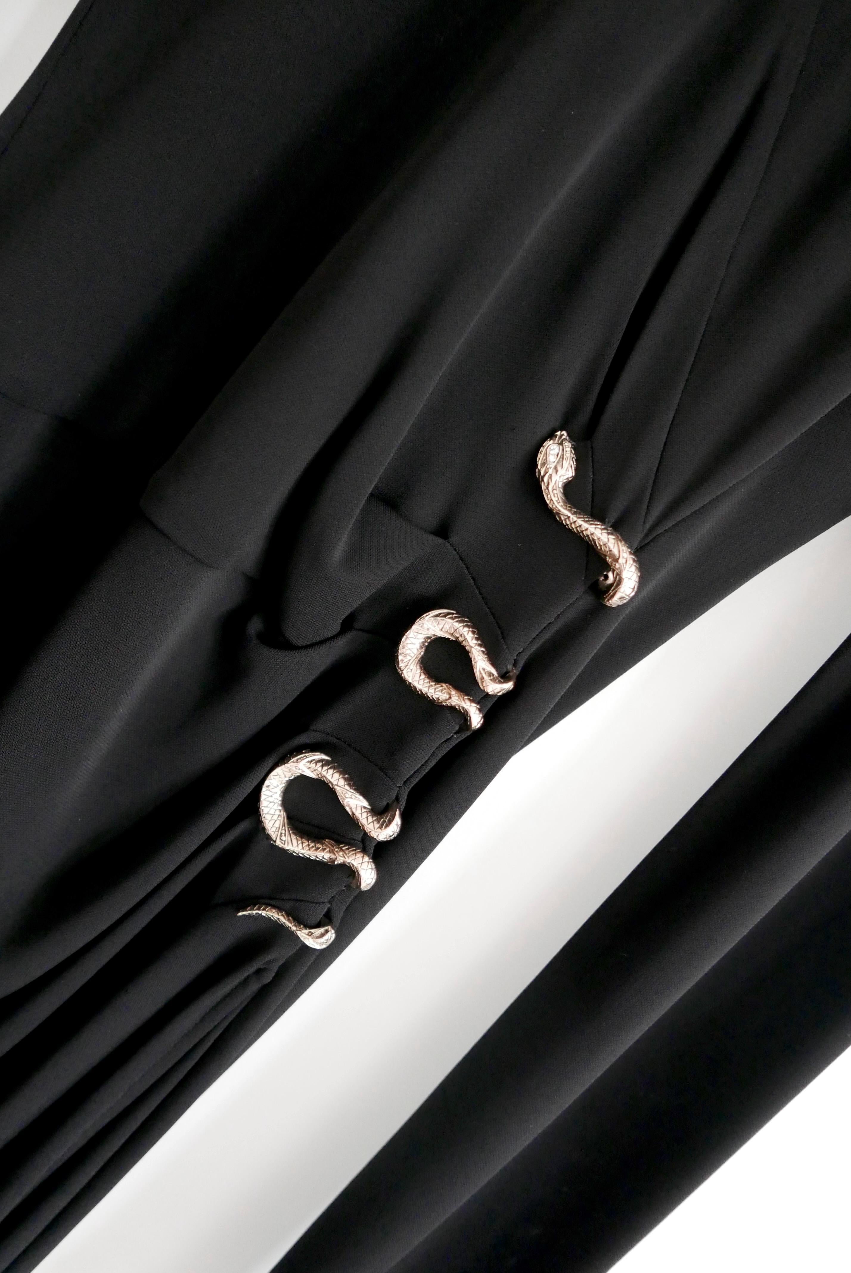 Fabuloso vestido negro de Roberto Cavalli con adornos de serpiente - usado una vez. Confeccionada en viscosa negra superelástica con adorno de serpiente metálica dorada en un lateral. Tiene un corte ajustado con manga larga y detalles fruncidos.