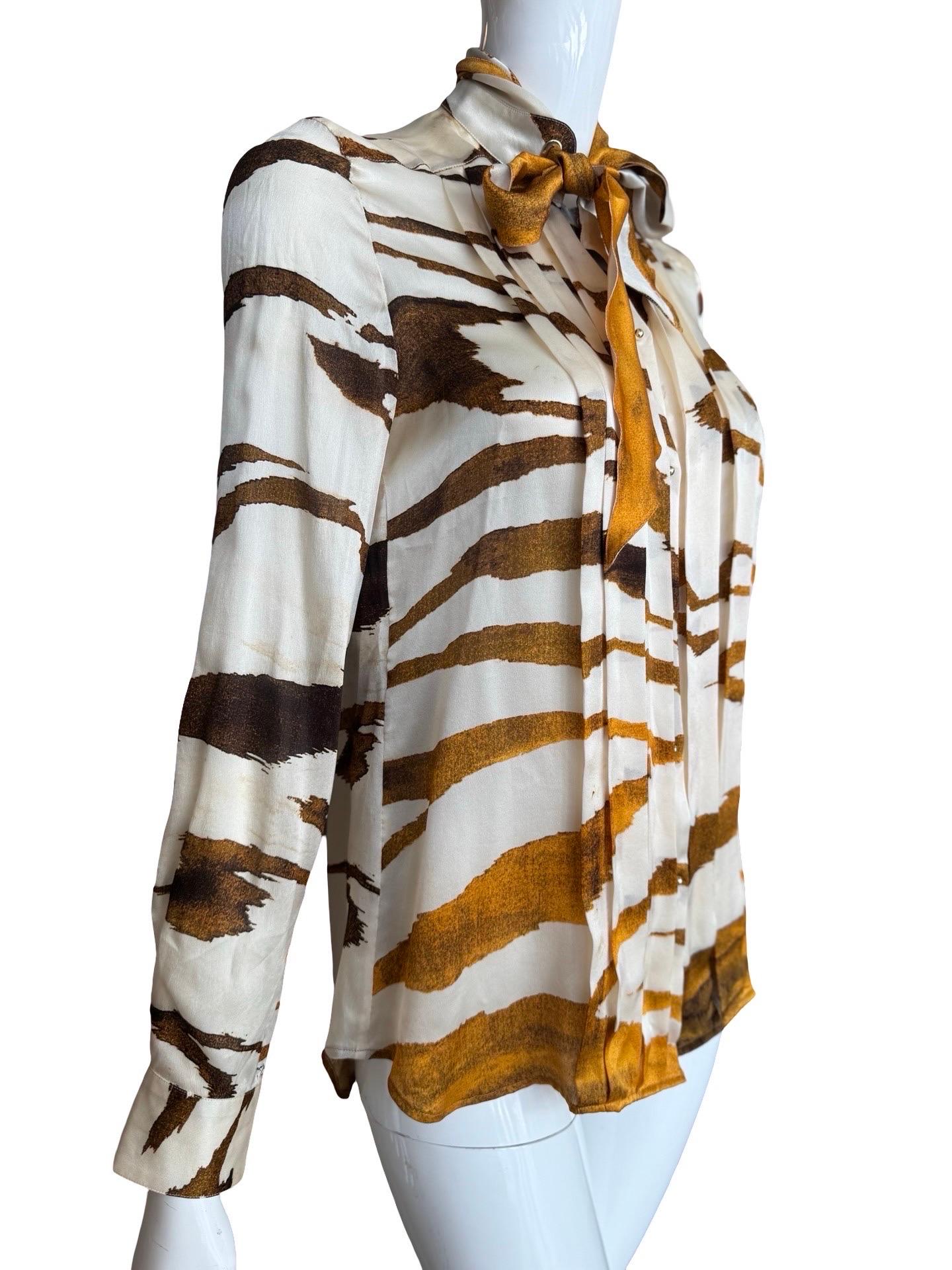 Modern classic Roberto Cavalli Silk blouse in an orange/brown tiger print.  The front of the blouse is pleated on either side of the buttons.  The buttons are small gold balls which snap closed.  The collar has a woven through piece of silk that can