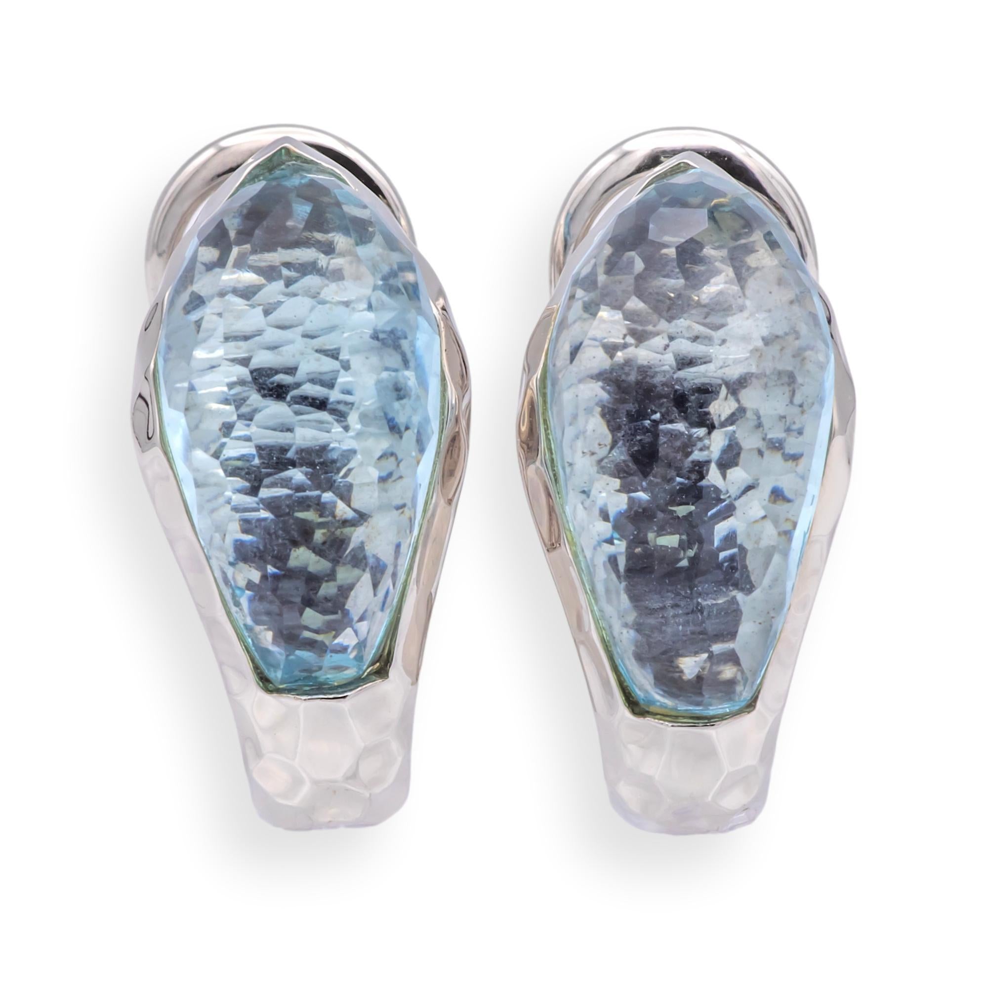 Boucles d'oreilles clip / post Roberto Coin en or blanc martelé 18K, ornées de pierres précieuses topazes bleues à facettes en serti clos totalisant environ 14 carats. Le design fluide et la finition texturée créent un mélange harmonieux entre le