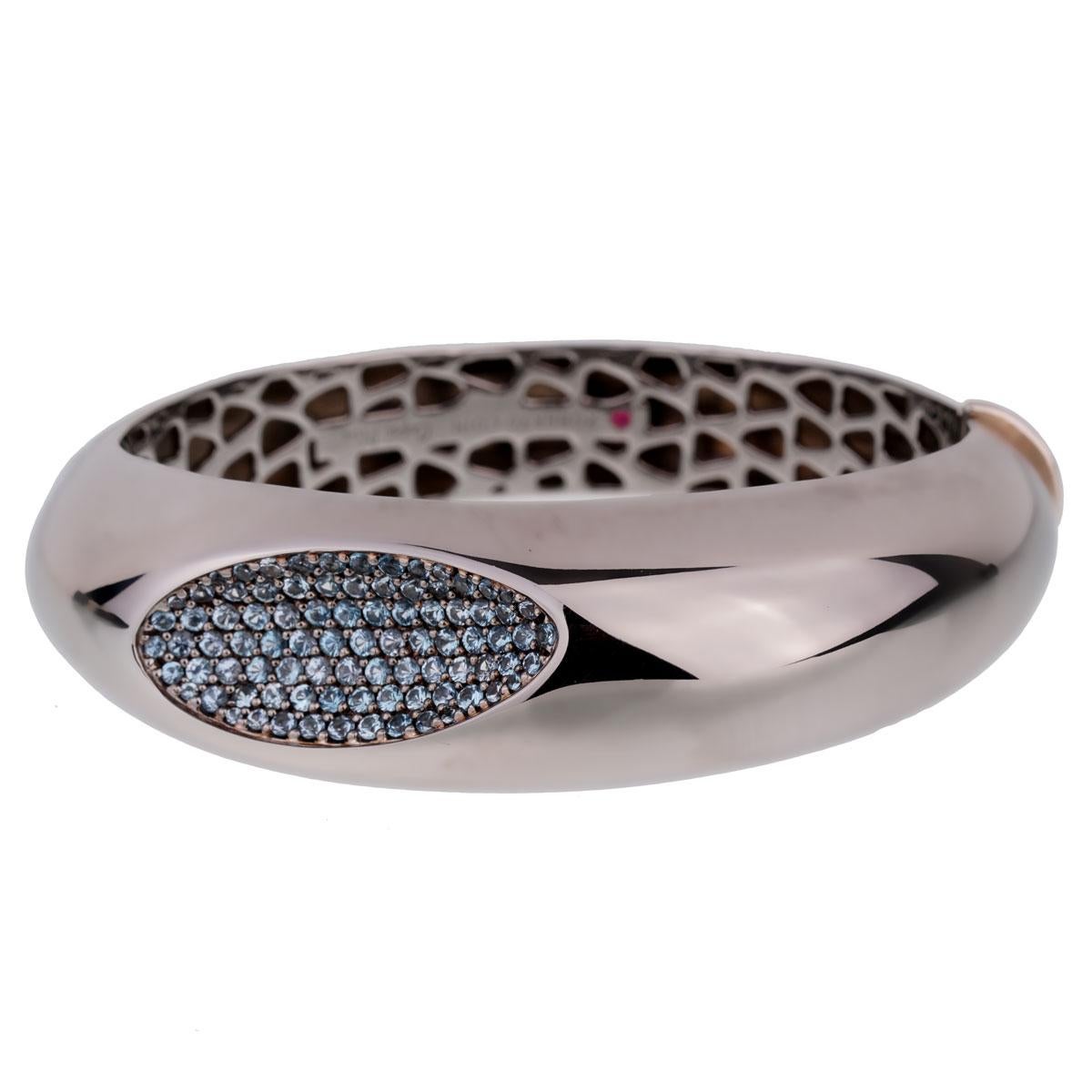 A chic Roberto Coin bangle bracelet from the Capri Plus collection set with round blue topaz in silver plated Ruthenium for a stunning gun metal color. 

The bracelet measures 6.5