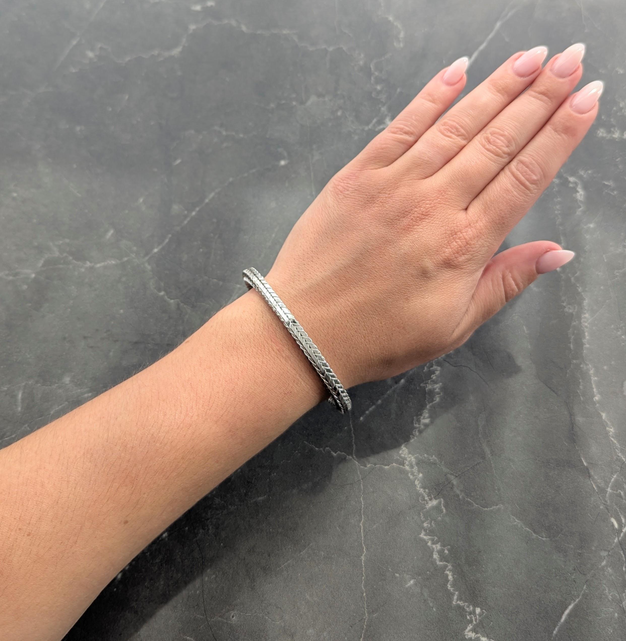 Bracciale aperto in stile polsino in oro bianco intrecciato.
Con un filo di ferro avvolto intorno a pannelli flessibili che raffigurano un motivo...
Terminazione con terminali a forma di cuscino con diamanti incastonati
Taglio rotondo brillante e
