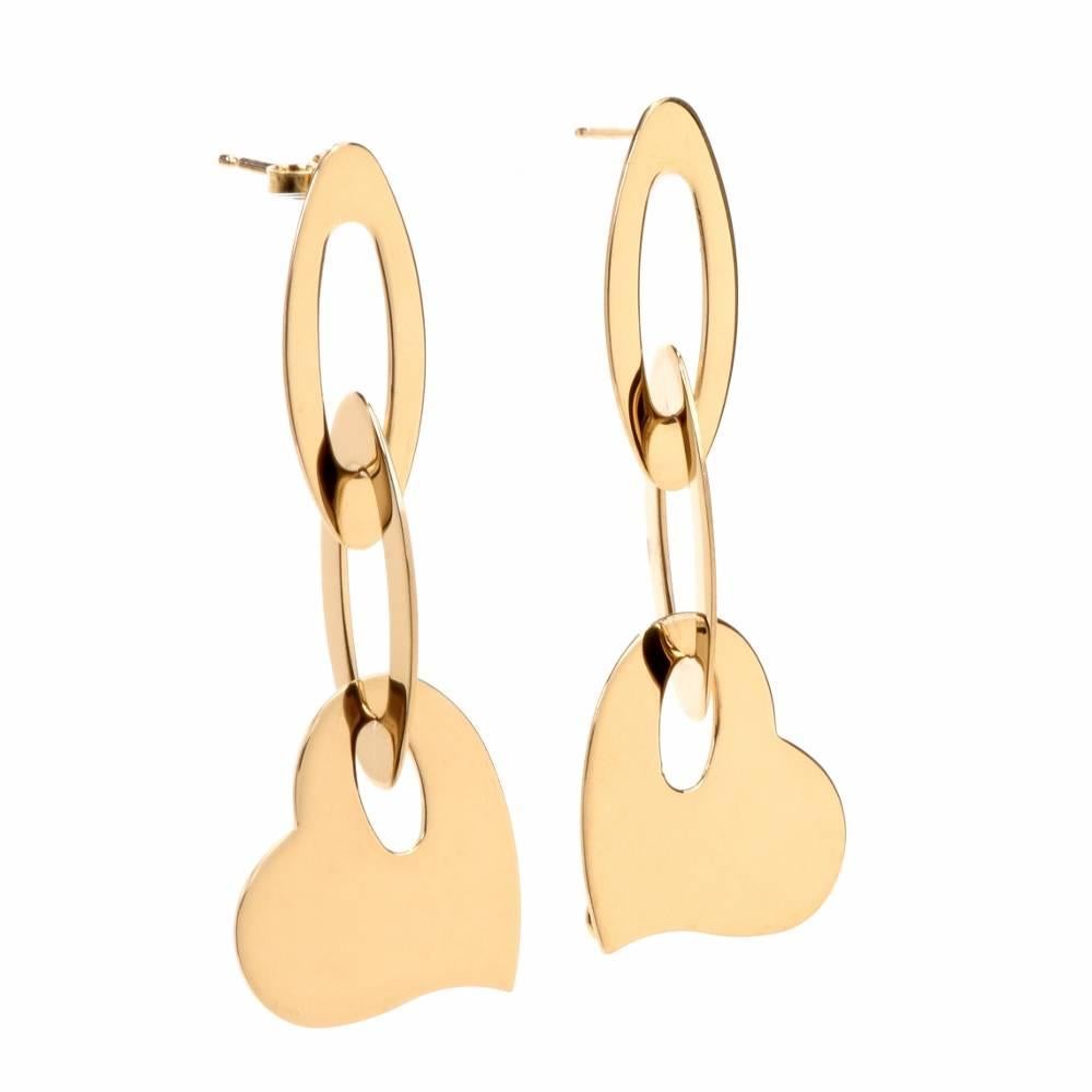 These Roberto Coin 18 karat yellow gold earrings weighing 10.8 grams and measuring 2 inches long and 20 mm wide comprise each a heart shape profile suspending from a pair of inversely interlocked ovular hoops, the upper one featuring a post. The