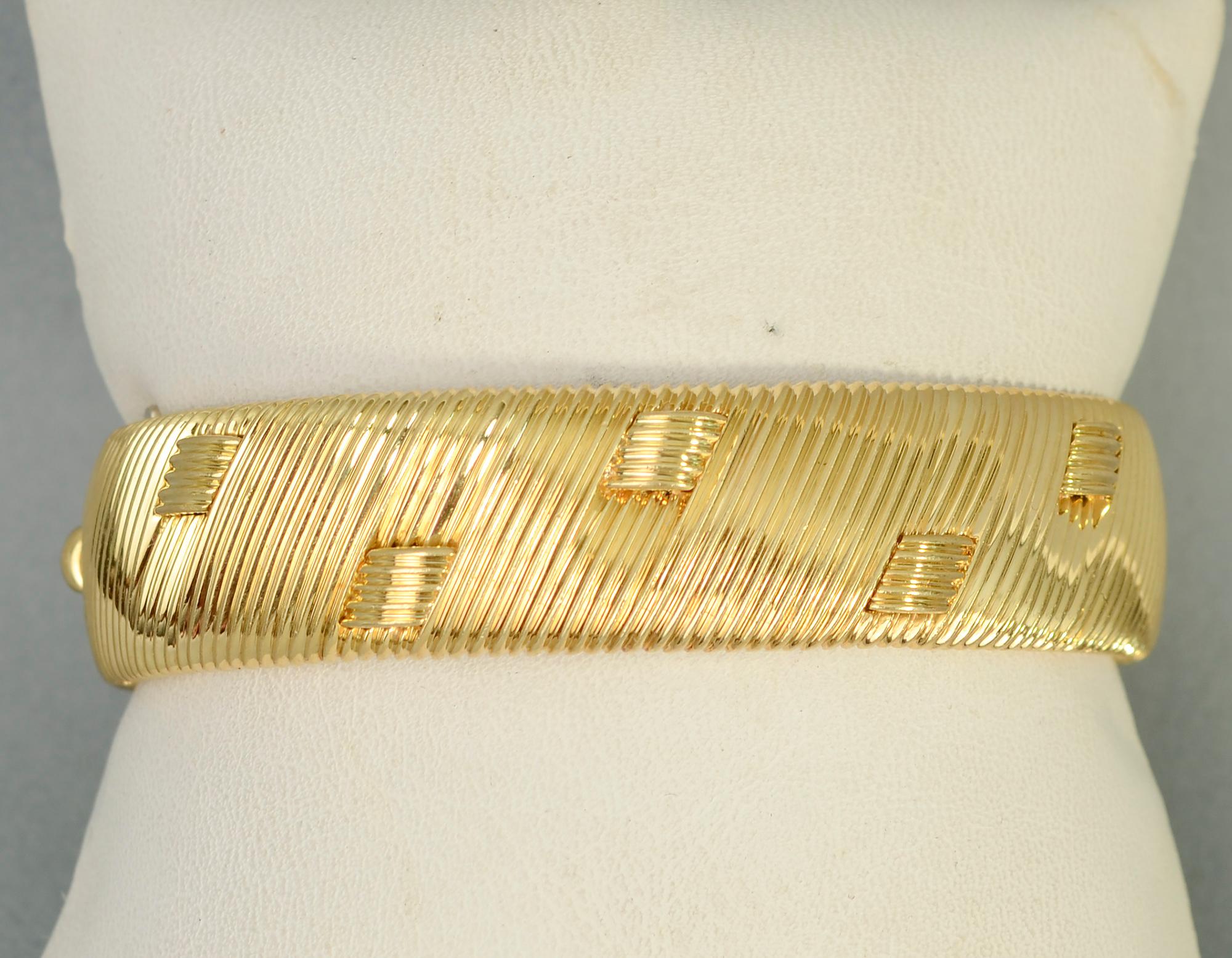 This hinged bangle bracelet by Roberto Coin is a most unusual design for him. Scored diagonal lines of gold are interspersed with small curved bands that appear as though they are woven through the gold.
The bracelet is 9/16