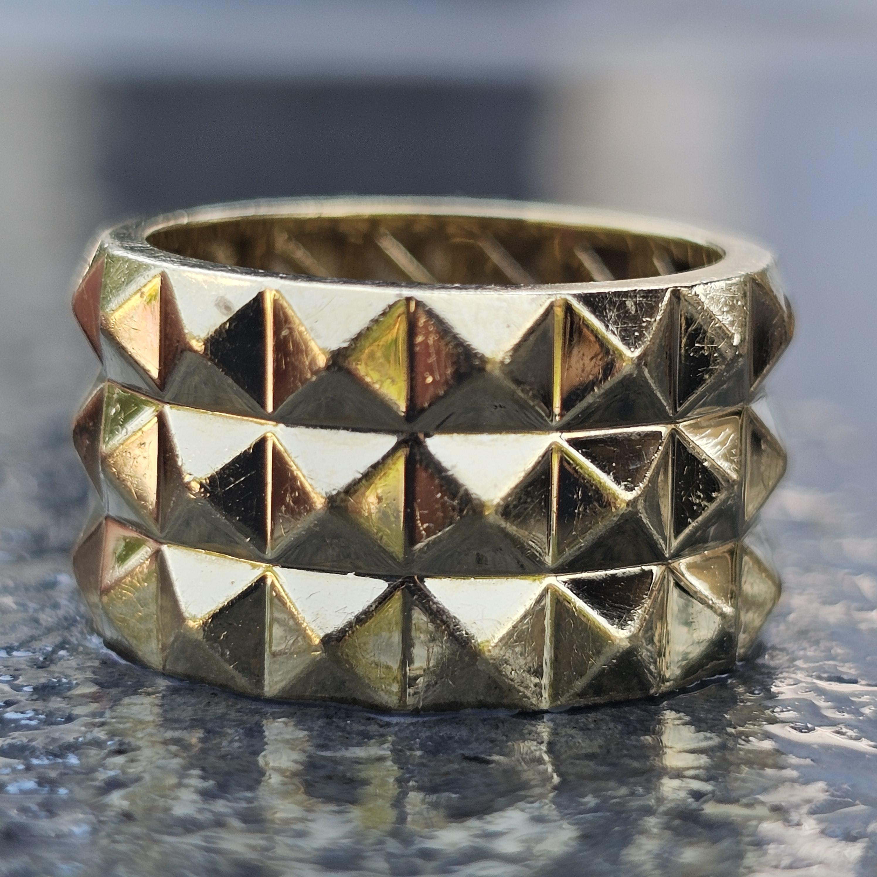 Cette magnifique bague à trois rangs de Roberto Coin Obelisco est une pièce captivante pour tout amateur de bijoux. Réalisée en luxueux or jaune 18 carats, cette bague présente un motif géométrique audacieux de clous pyramidaux en relief. Le design