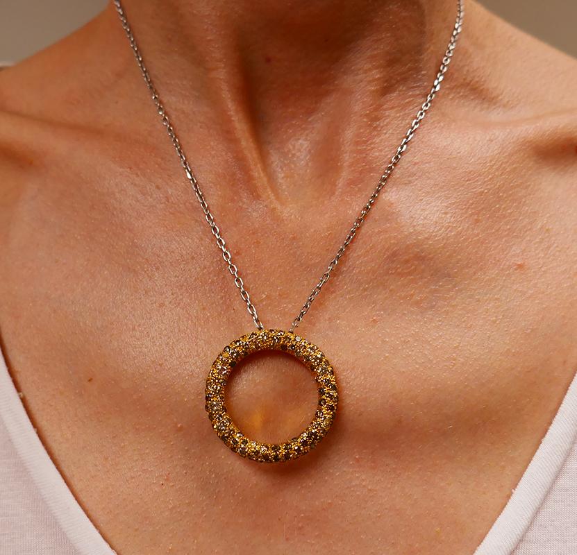 A Roberto Coin Circle pendant and chain, made of 18 karat yellow gold featuring fancy colored diamonds.
White and fancy colored diamonds are staged in textured gold circle pendant. It’s hollow and pierced with the floral design on the back. The