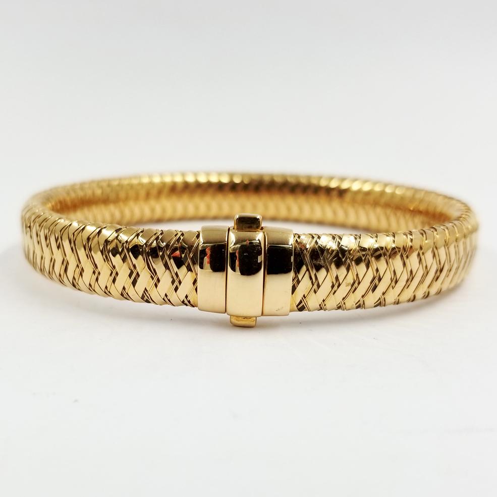 This flexible 18 karat rose gold bracelet is from the Roberto Coin Primavera Collection. The 9mm wide bracelet design is comprised of woven gold around a central flat tube. The inside of the double pusher clasp is stamped 