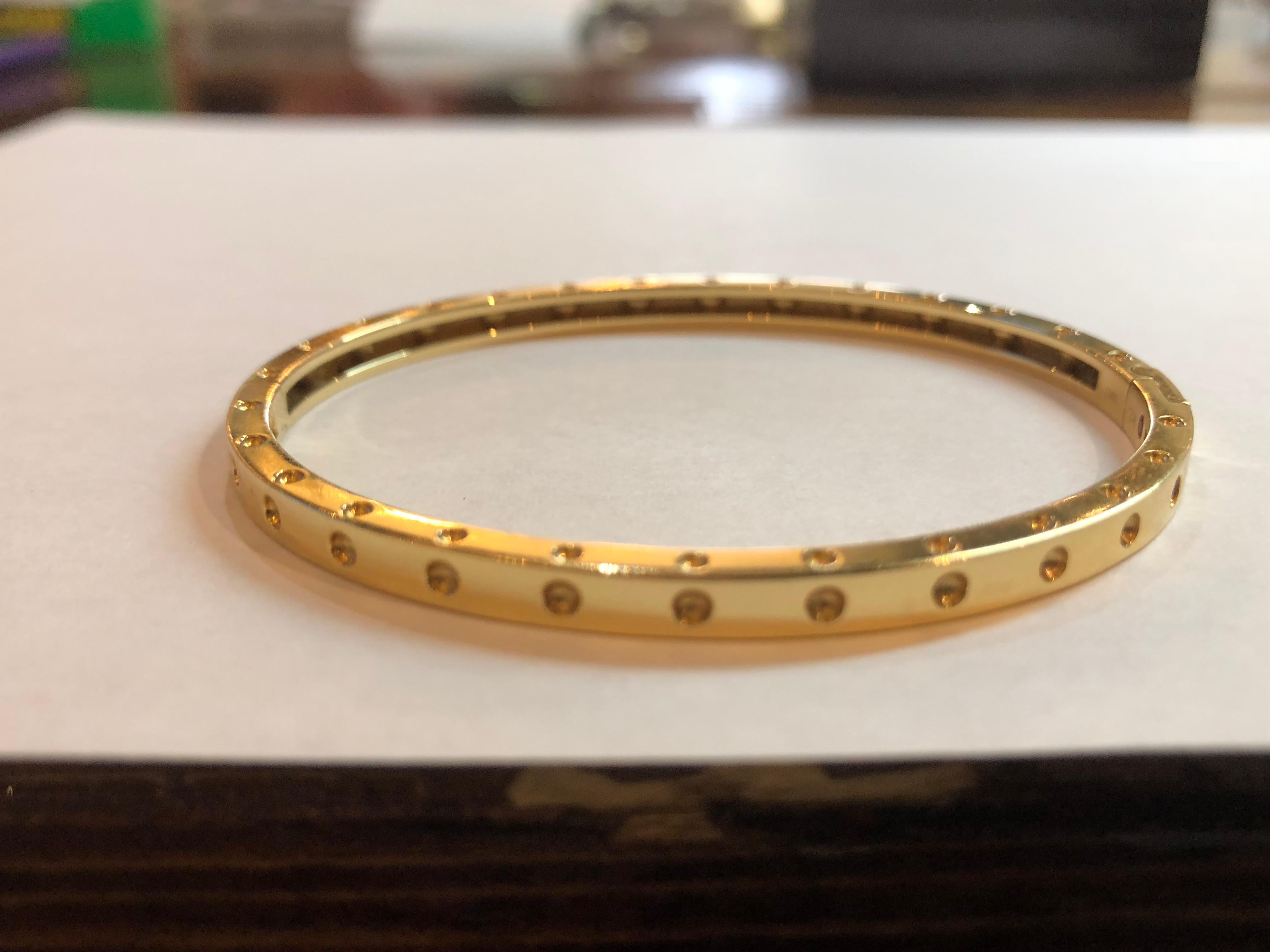 From the Symphony Pois Moi Collection this beautiful bangle is a great accent piece. Its forged in 18k gold and has small divots that grace the top and the sides to give this piece a cosmopolitan. this stunning bangle from Robetro Coin can be