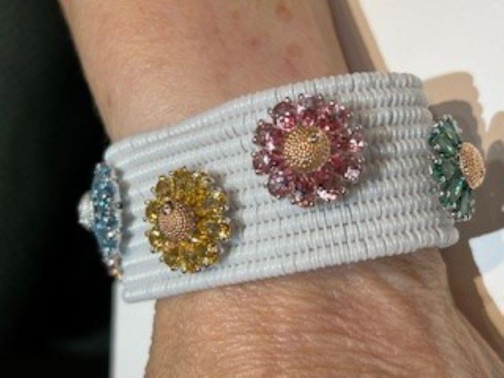 White ceramic expandable bracelet with 8 flower stations by Roberto Demeglio.  The flower stations are composed of ten pear shaped topaz with a center button feature a .01ct round diamond.  Each flower station measures 18mm in diameter.   The width
