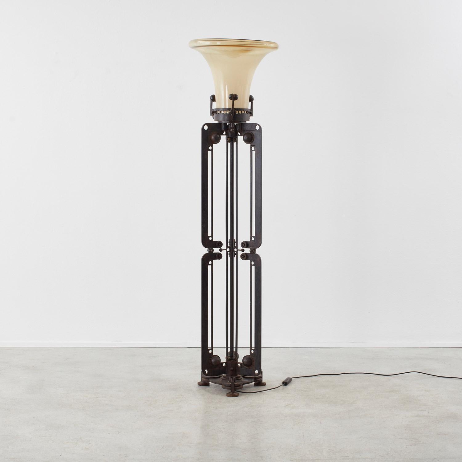 Una pantalla de cristal de Murano en forma de embudo emerge de un artilugio de hierro forjado en esta anacrónica pieza de Roberto Fallani (n. 1937). El diseño cinético sugiere una función mecánica desconocida, con su lenguaje de pernos, cojinetes de