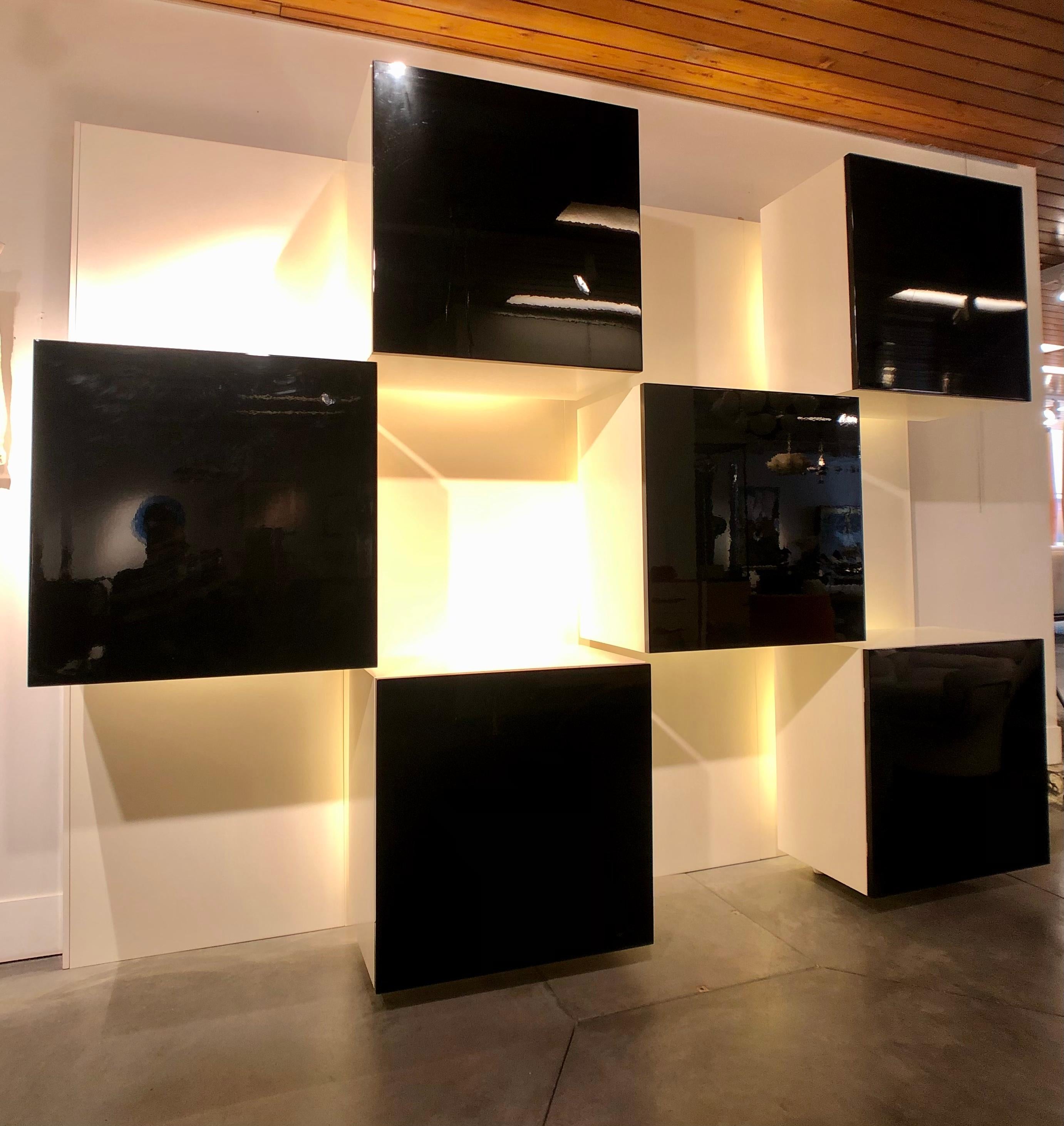 Roberto Monsani pour Acerbis, unité murale lumineuse 
6 boîtes noires munies chacune d'une lumière et fixées sur 4 panneaux muraux blancs avec quelques fixations en plexi donnant une impression de mobilier flottant.
Bon état général une trace est