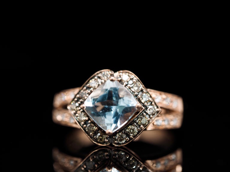This Roberto Ricci rose gold ring is a timeless piece. Set in 14 karat rose gold, with an amazing light blue topaz as the center stone. A halo with brown/chocolate diamonds delicately wraps around the center gem, and diamonds dripping down the band,