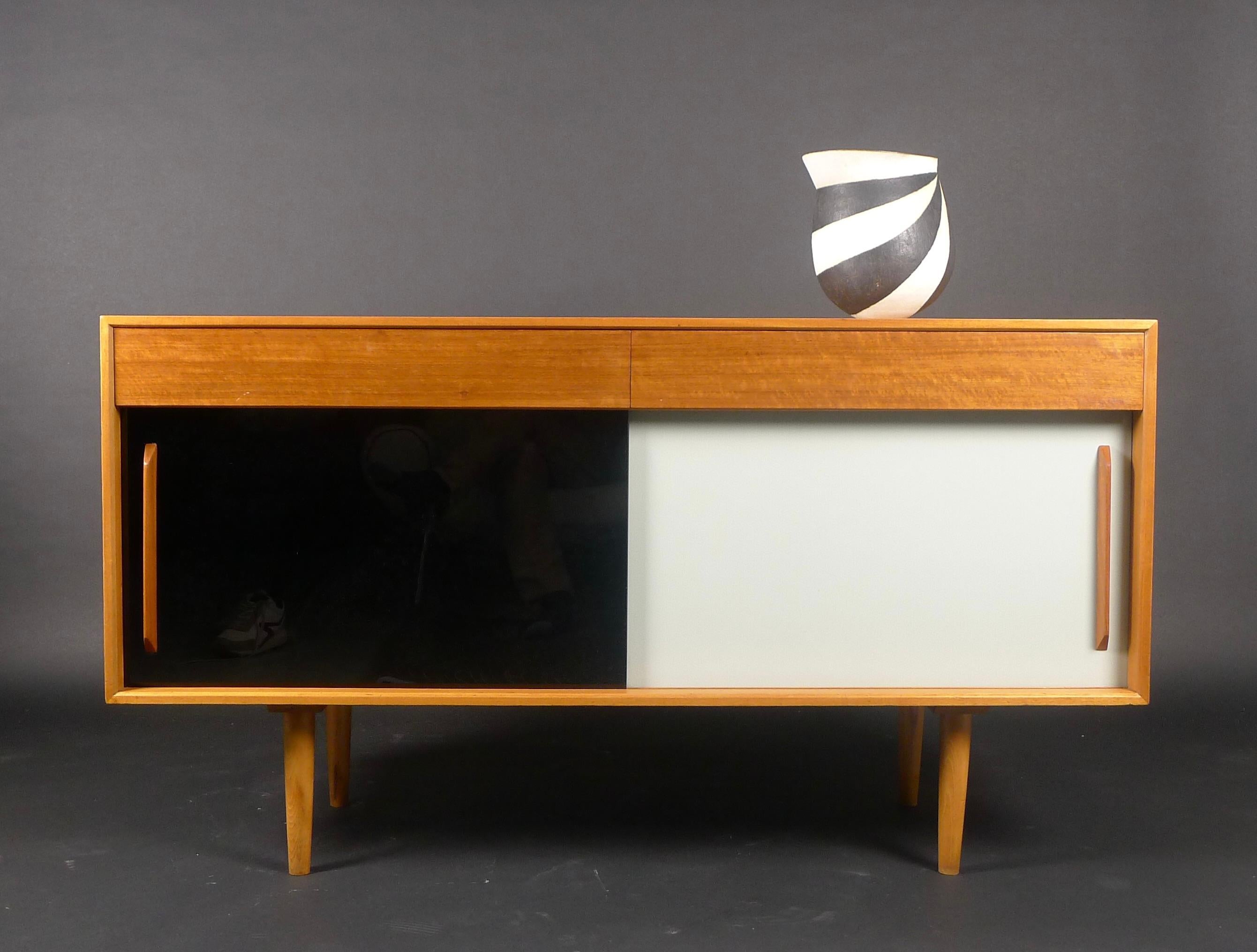 Robin Day, a 'Hilleplan' unit B sideboard, designed circa 1953 for Hille, walnut cased cabinet with two short drawers above two sliding cupboard doors in black and white vitrolite, raised on tapering wood feet, Hille label to drawer