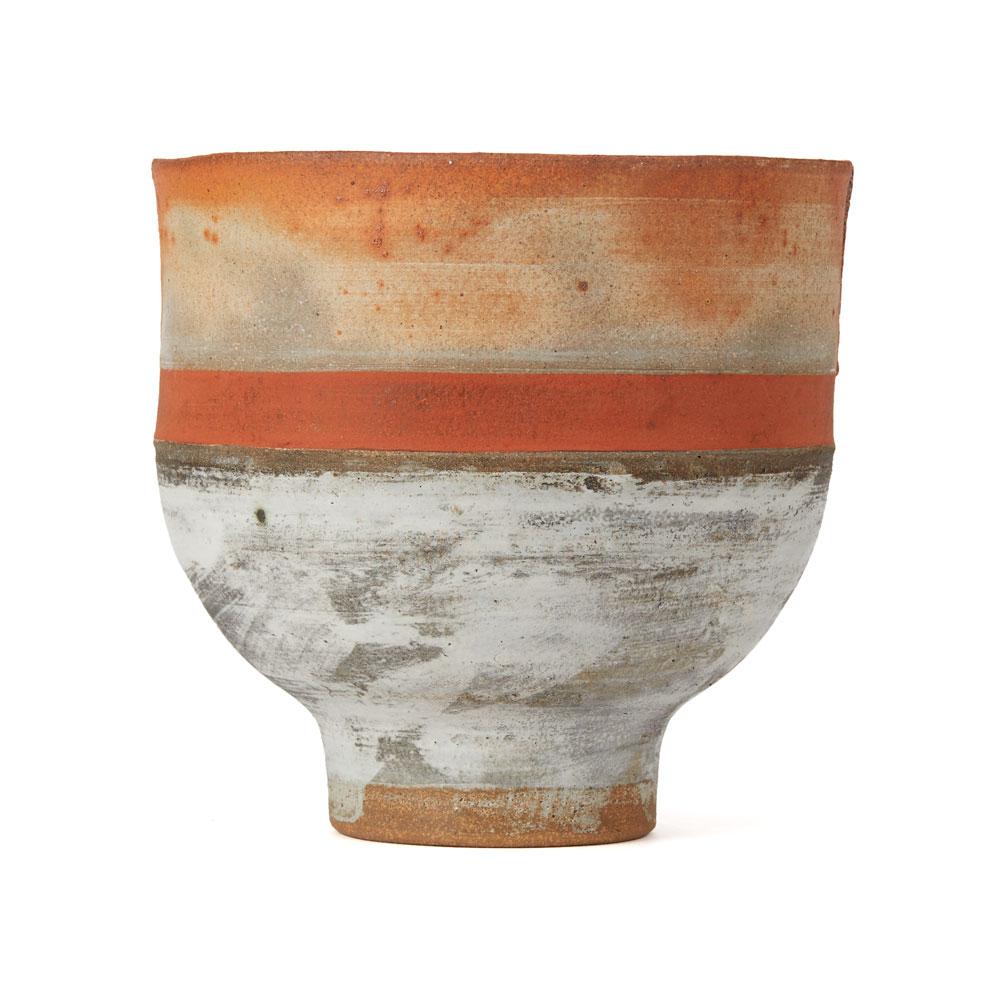A vintage British studio pottery stoneware footed bowl by Robin Welch. The rounded bowl stands on a narrow rounded foot, the rim with opposing incisions and is glazed with an orange band with buff and grey ashen glazes above and below. The bowl is