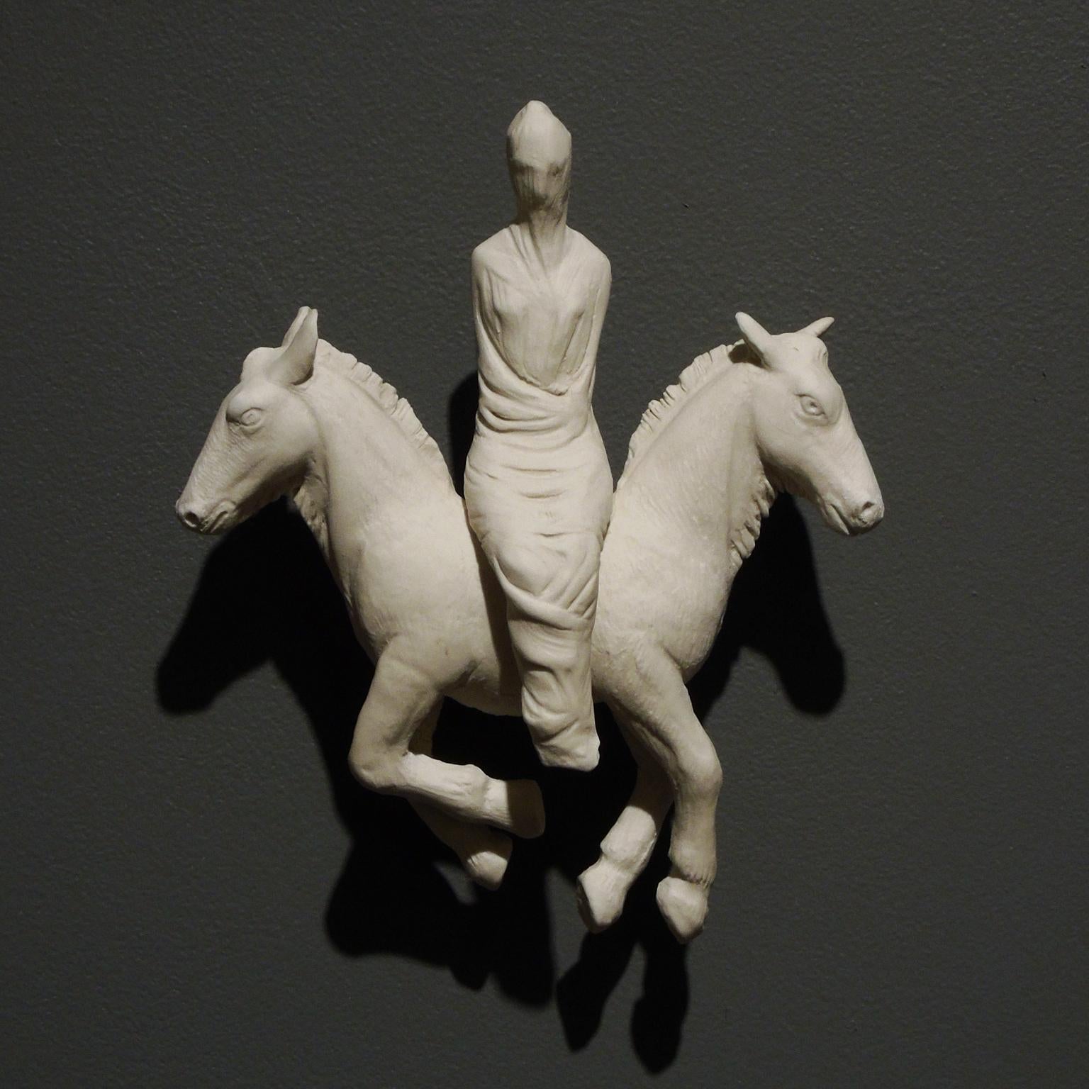 "Shroud" a white porcelain sculpture by Robin Whitman, features a wrapped female figure seated on the back of a two headed donkey, The two donkey heads are at the opposite ends of the beast. Whiteman's work employs human and animal imagery to