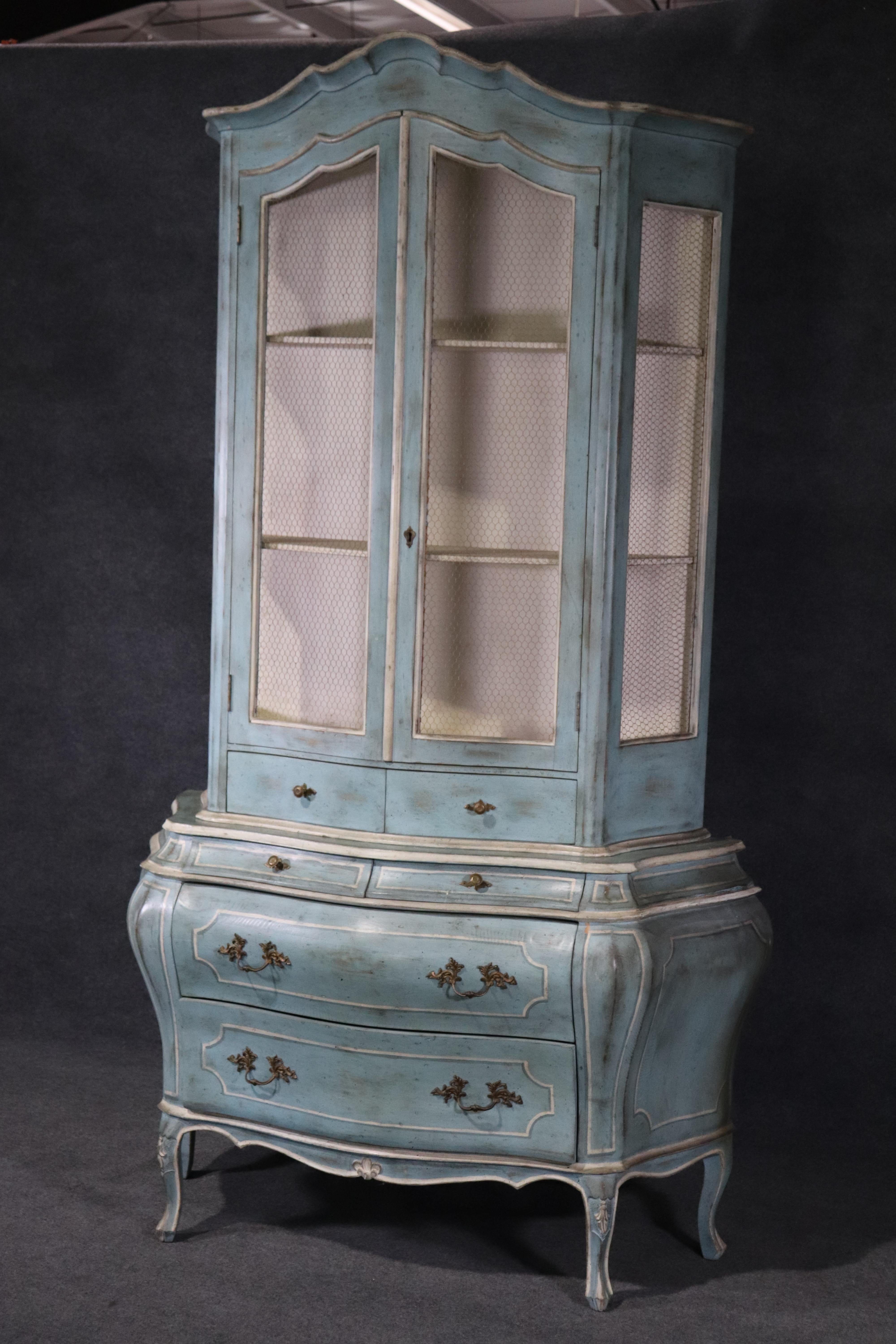 This is a stunning antique paint decorated china cabinet from Italy. The cabinet has a gorgeous blue exterior and an antique glaze on top. The doors have an open mesh wire system. This is an eye catching piece and dates to the 1950s. Measures 88