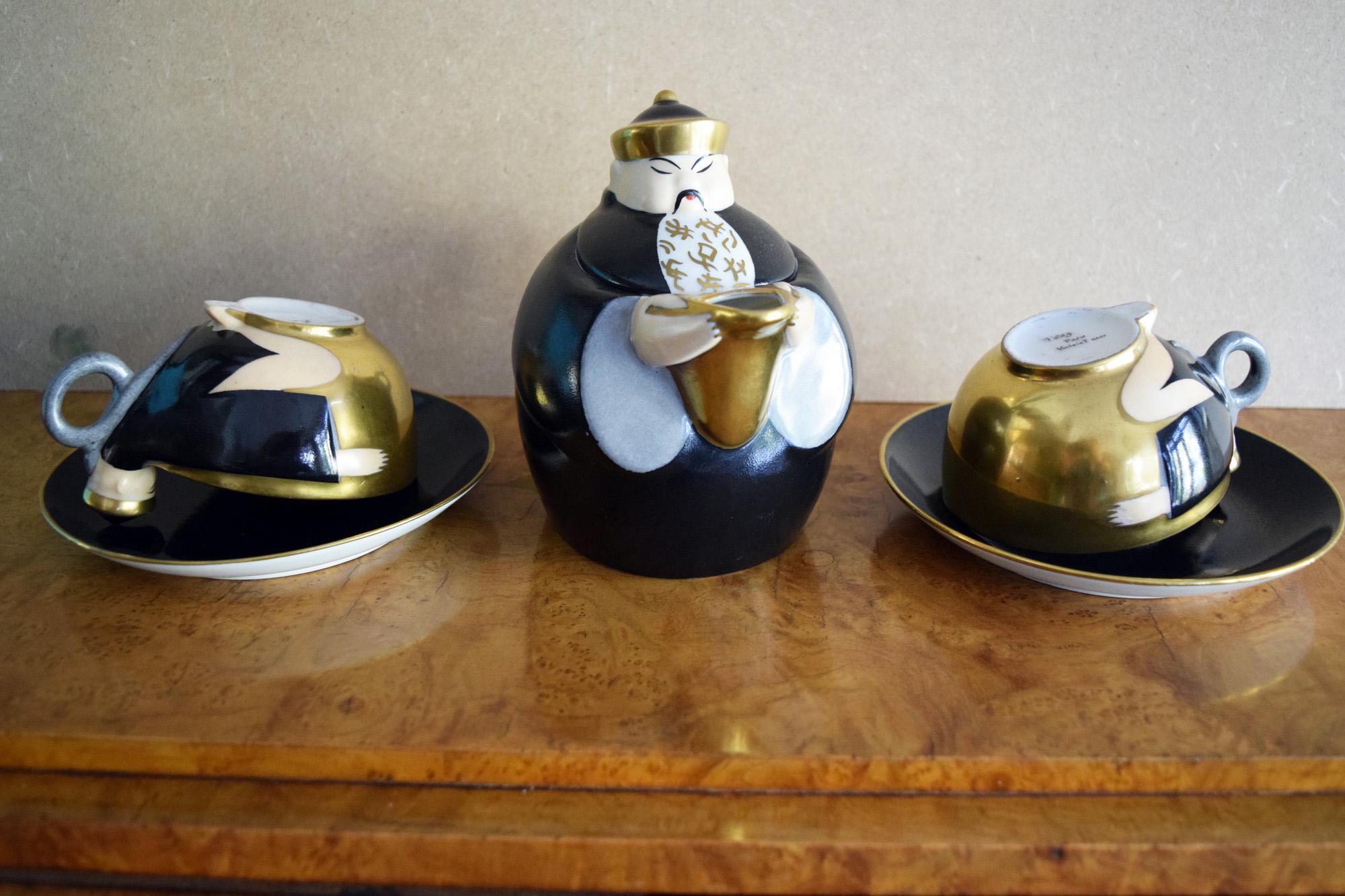 Robj porcelaine Chinese character bachelor tea set
A three piece rare tea set by Robj comprising a Chinese man as a tea pot  in navy blue wearing a gilt hat,  gilt spout. There are two cups and saucers in navy blue ,gold and white depicting two