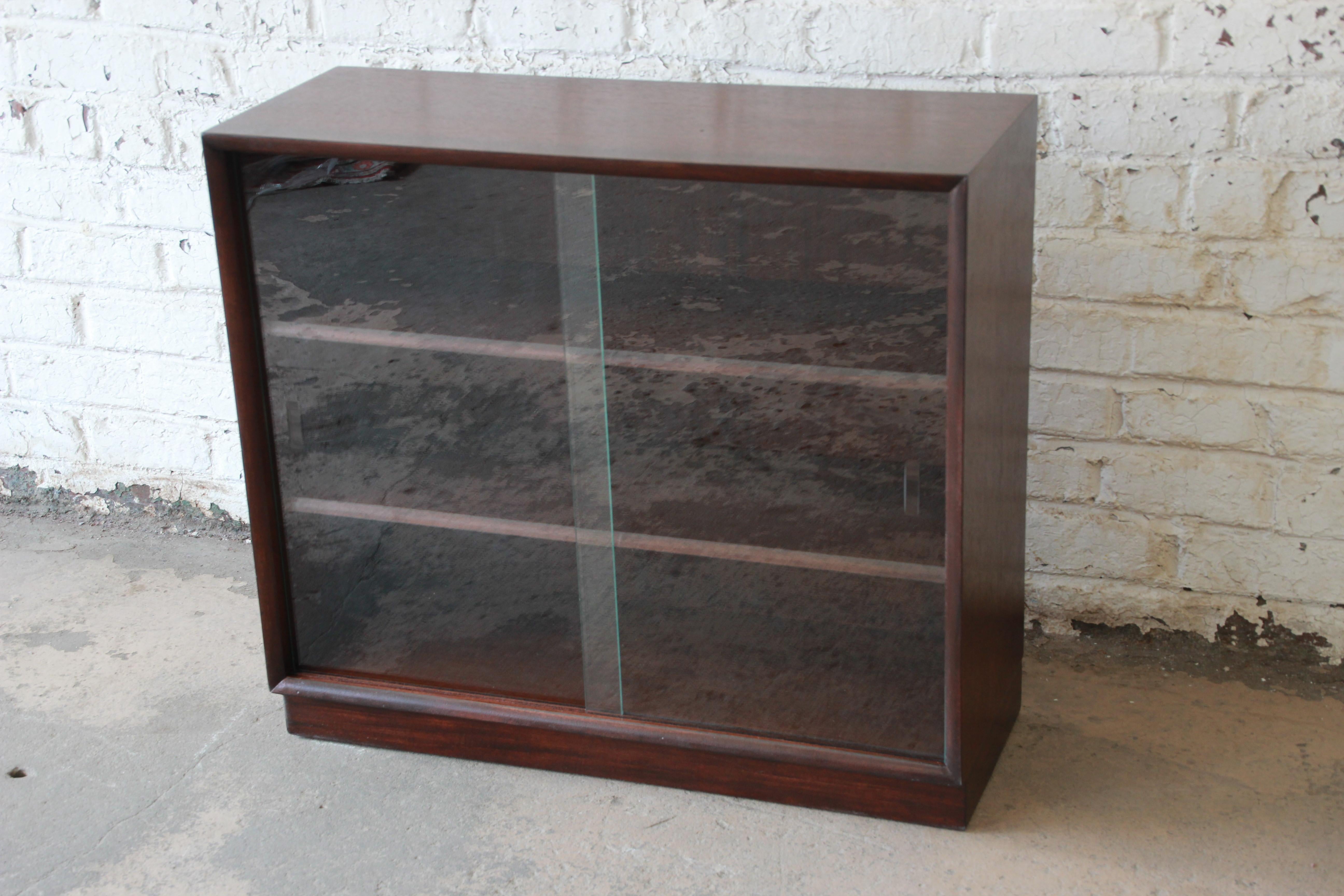 A very nice Mid-Century Modern glass front bookcase designed by T.H. Robsjohn-Gibbings for Widdicomb. The bookcase features a clean and simple midcentury design. It has two sliding glass doors and two adjustable shelves for book storage or display.