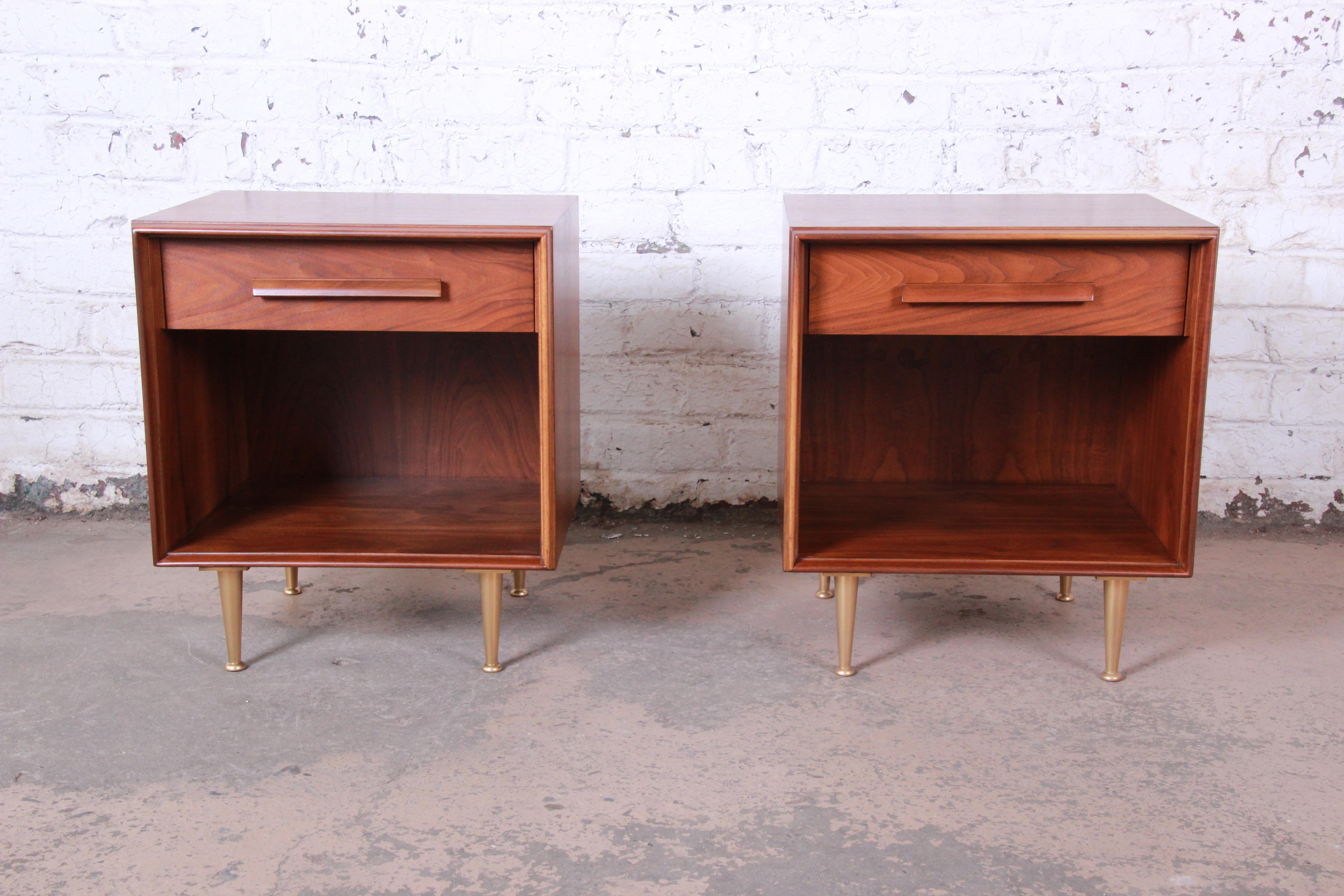 An exceptional pair of Mid-Century Modern nightstands or side tables designed by T.H. Robsjohn-Gibbings for Widdicomb circa 1950. The nightstands feature gorgeous walnut wood grain and sleek mid-century design. The walnut cases sit on brass-finished