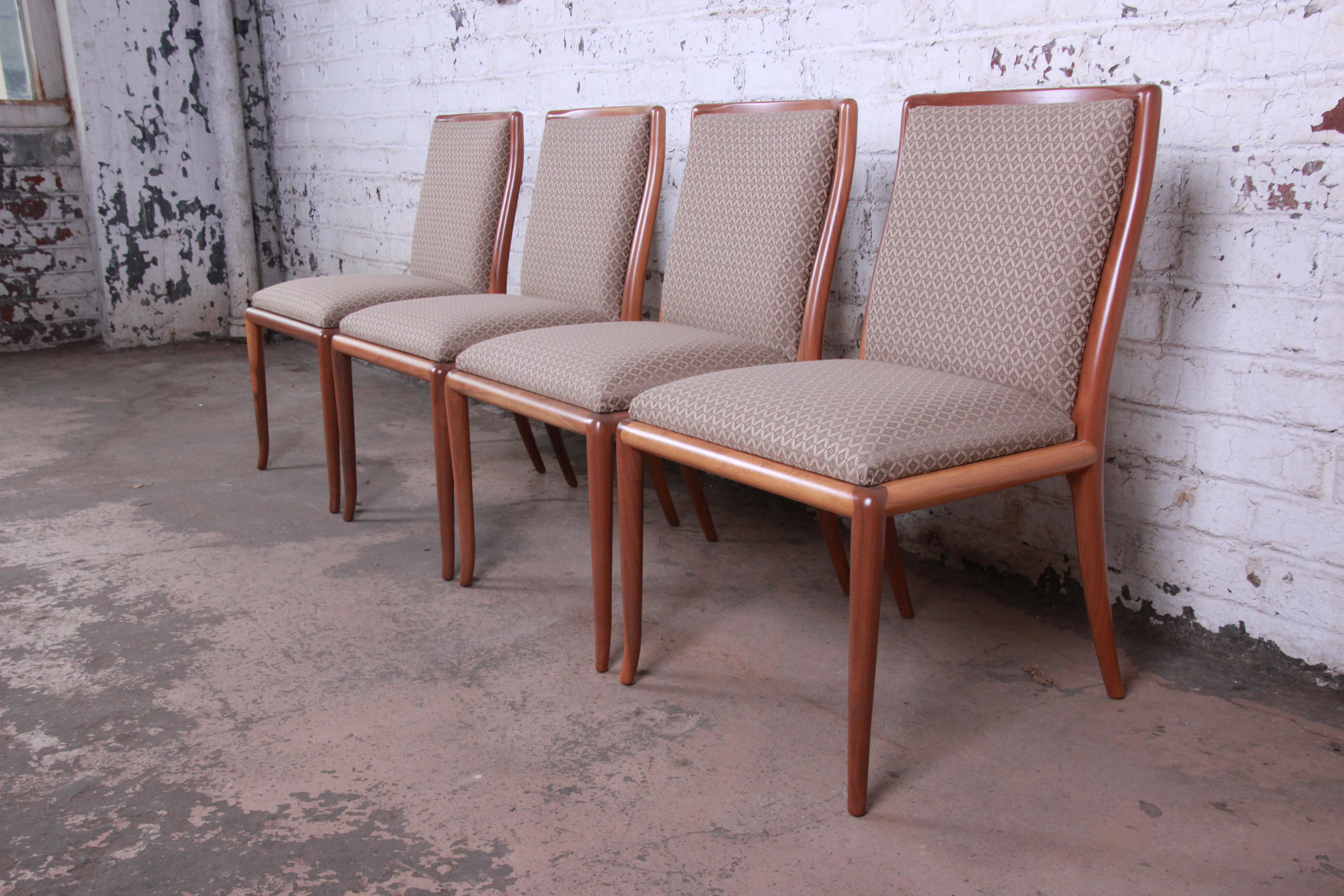 An outstanding set of four Mid-Century Modern saber leg dining chairs designed by T.H. Robsjohn-Gibbings for Widdicomb. The chairs feature gorgeous sculpted solid walnut frames with a unique saber leg design. The beige and red upholstery is clean