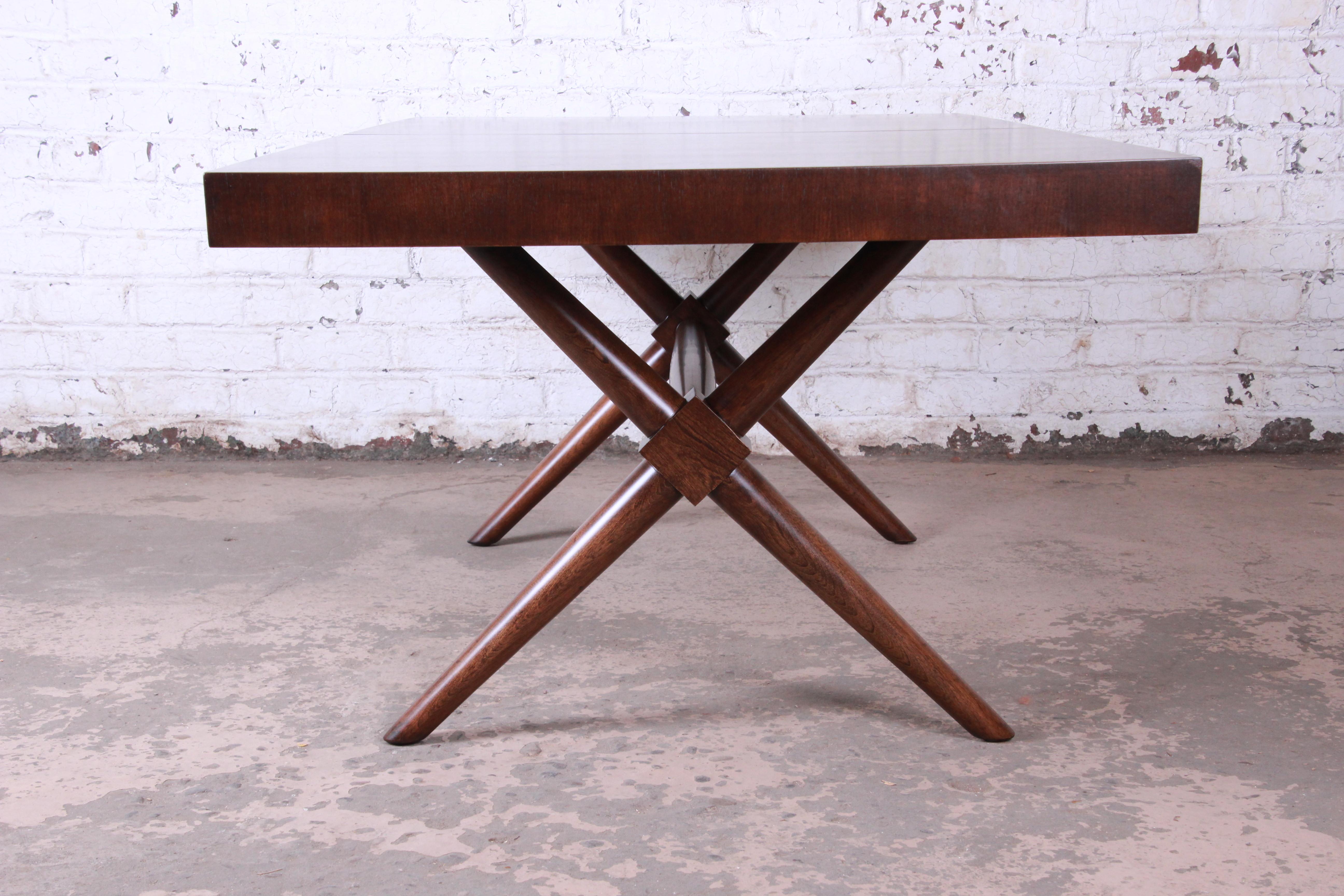 An exceptional Mid-Century Modern X-base walnut dining table designed by T.H. Robsjohn-Gibbings for Widdicomb. The table features an iconic x-base design and stunning walnut wood grain. It measures 72