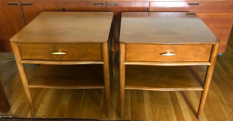 c. 1955, American, these handsome shaped squarish two-tiered tables each have a single drawer and wonderfully figured old growth walnut veneer. The versatile size make these perfect for end tables or nightstands. Finished on the back to allow