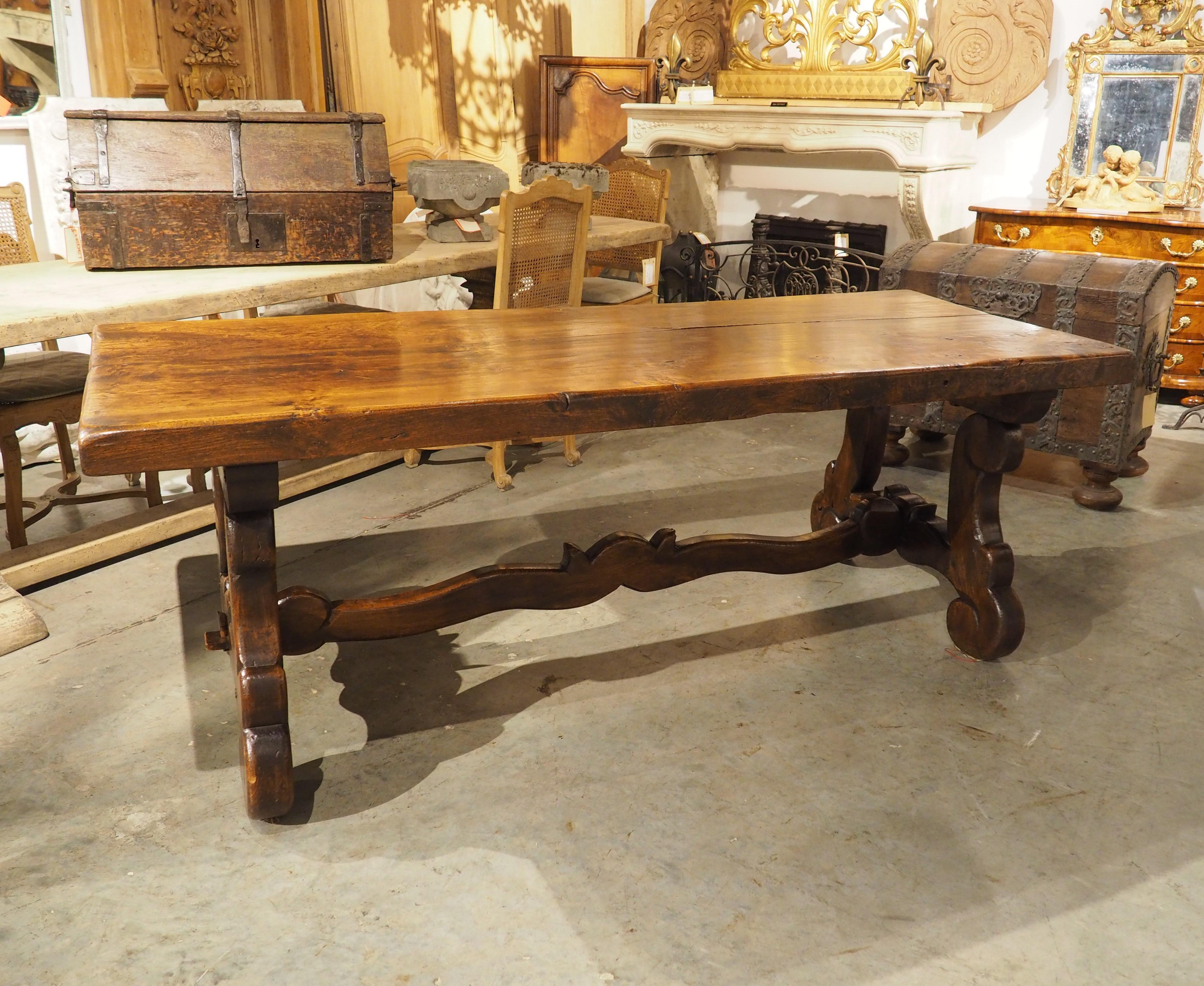 Hand-carved in Spain in the early 1900s, this elm dining table has a robust three-inch thick top. The beautiful table is accentuated by a rich, deep brown patina and large, open lyre legs embellished with voluminous scrolled and fretted motifs. A